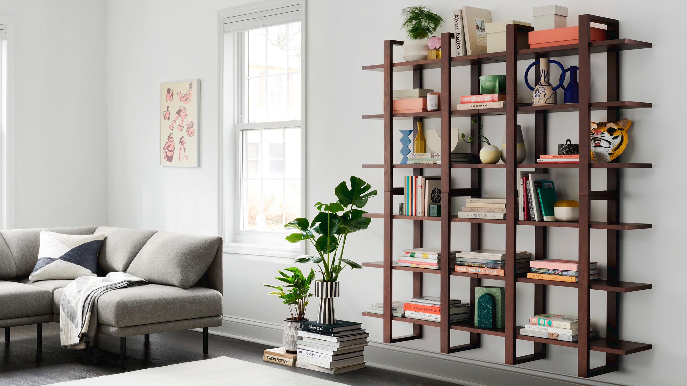 Modern living room with a wooden open bookshelf filled with books, plants, and decorative items next to a gray sectional sofa.
