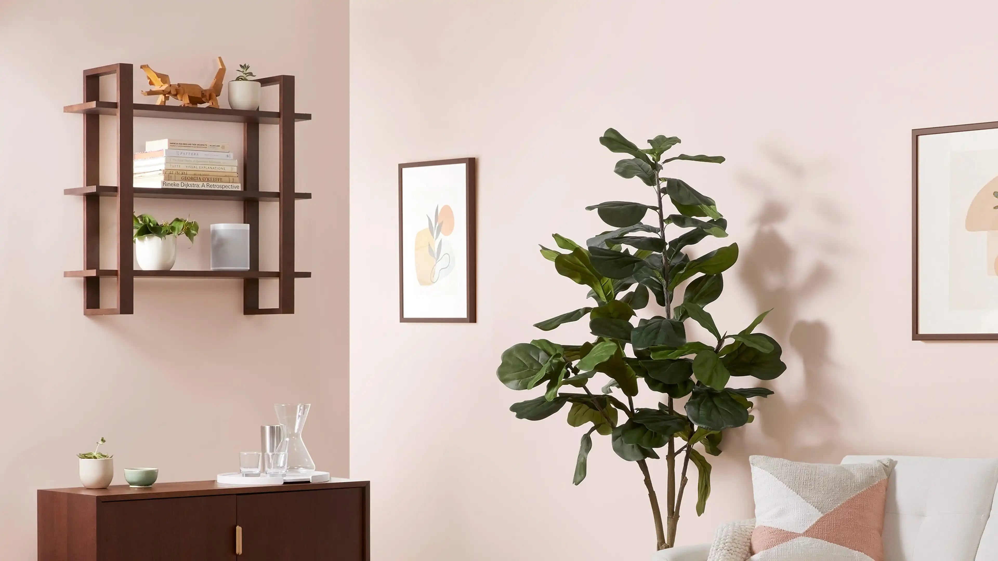 Wooden wall-mounted shelf with books, plants, and decorative items above a wooden cabinet with glassware in a softly lit living room.