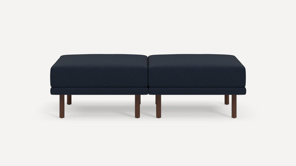 Two navy blue cushioned ottomans with dark wooden legs placed side by side on a plain white background.