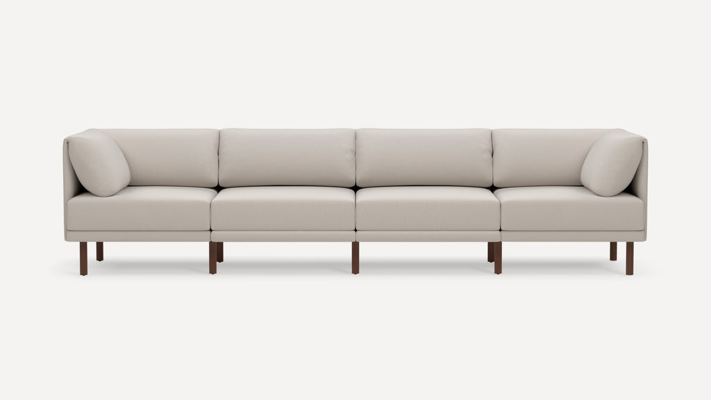 Modern four-seater beige fabric sofa with clean lines, cushioned backrests, arm pillows, and dark wooden legs on a white background.