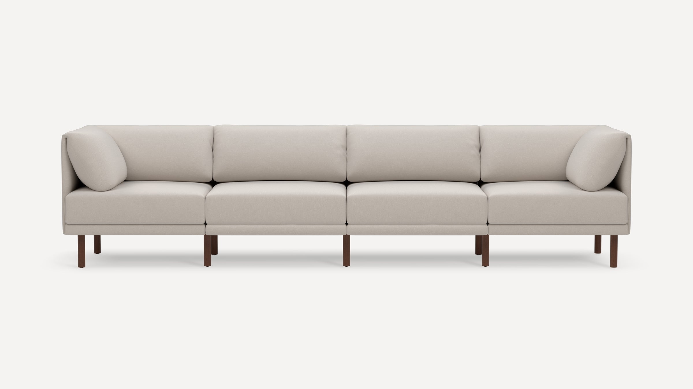 Modern four-seater beige fabric sofa with clean lines, cushioned backrests, arm pillows, and dark wooden legs on a white background.