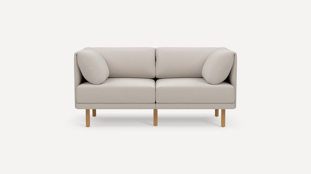 Modern two-seater sofa in light beige fabric with rounded cushions and wooden legs on a plain white background.