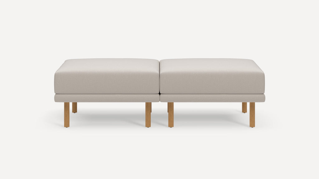Two beige rectangular cushioned ottomans with wooden legs placed side by side on a plain white background.