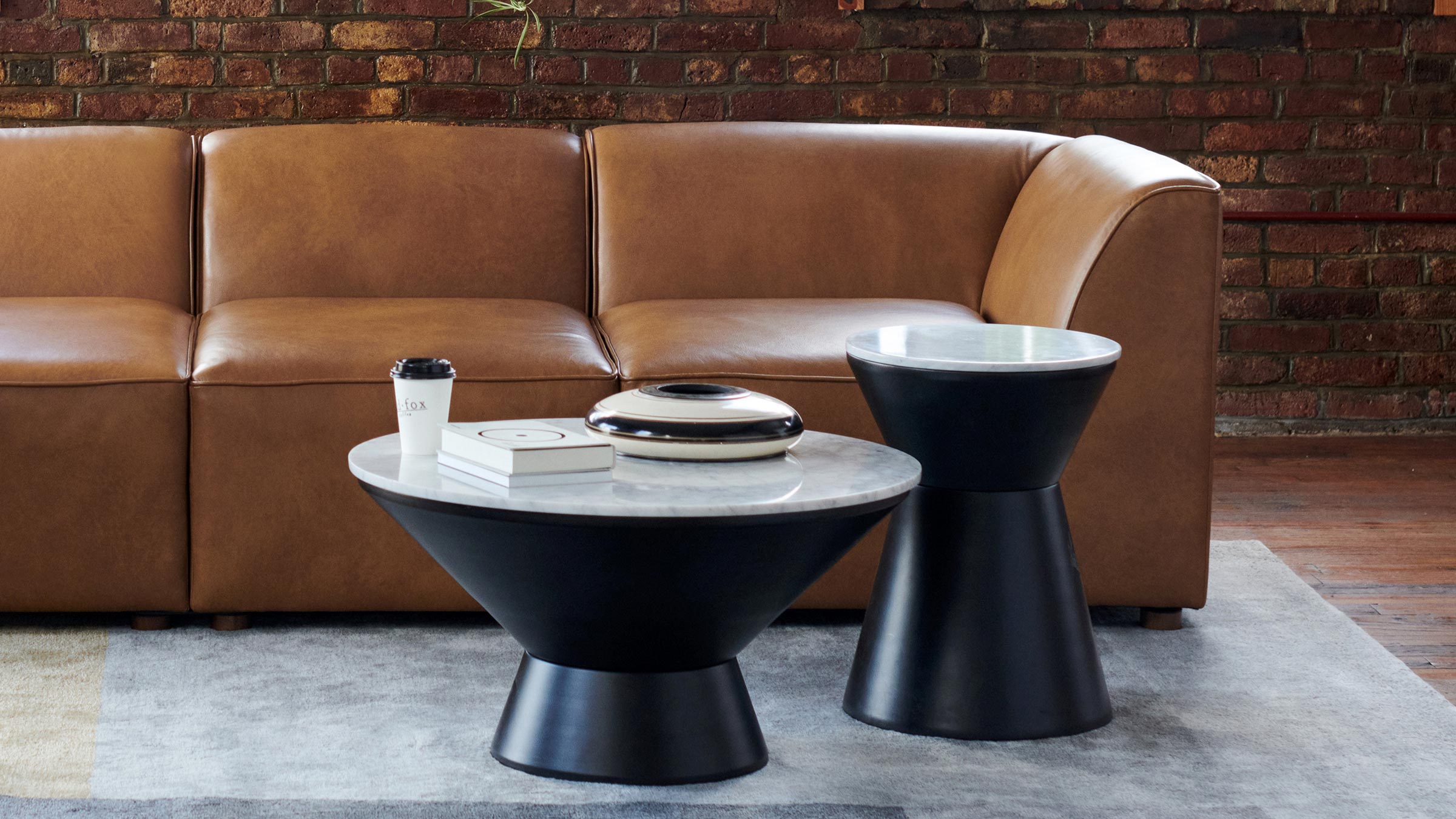 Set of two modern black metal and white marble top side tables, styled with books, decorative object, and coffee cup.