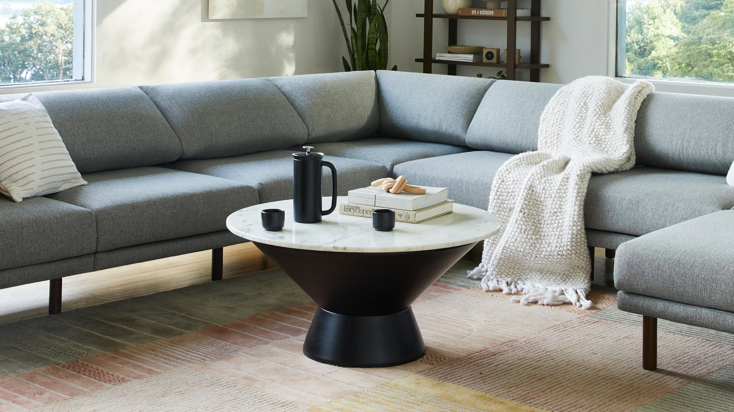 Round coffee table with a white marble top and black hourglass-shaped base, styled with books, a black coffee pot, and cups.
