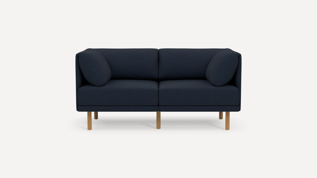 Modern navy blue two-seater sofa with rounded arm pillows and light wooden legs on a plain white background.