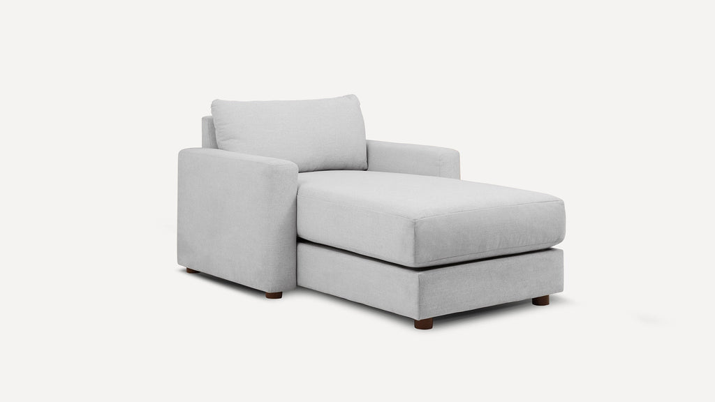 Light gray upholstered chaise lounge with cushioned backrest and armrest, supported by short wooden legs.