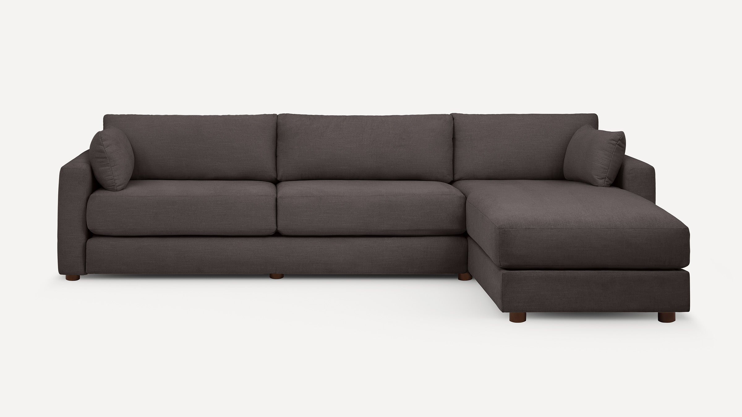 Large modern dark gray sectional sofa with chaise, plush cushions, and wooden legs on white background.