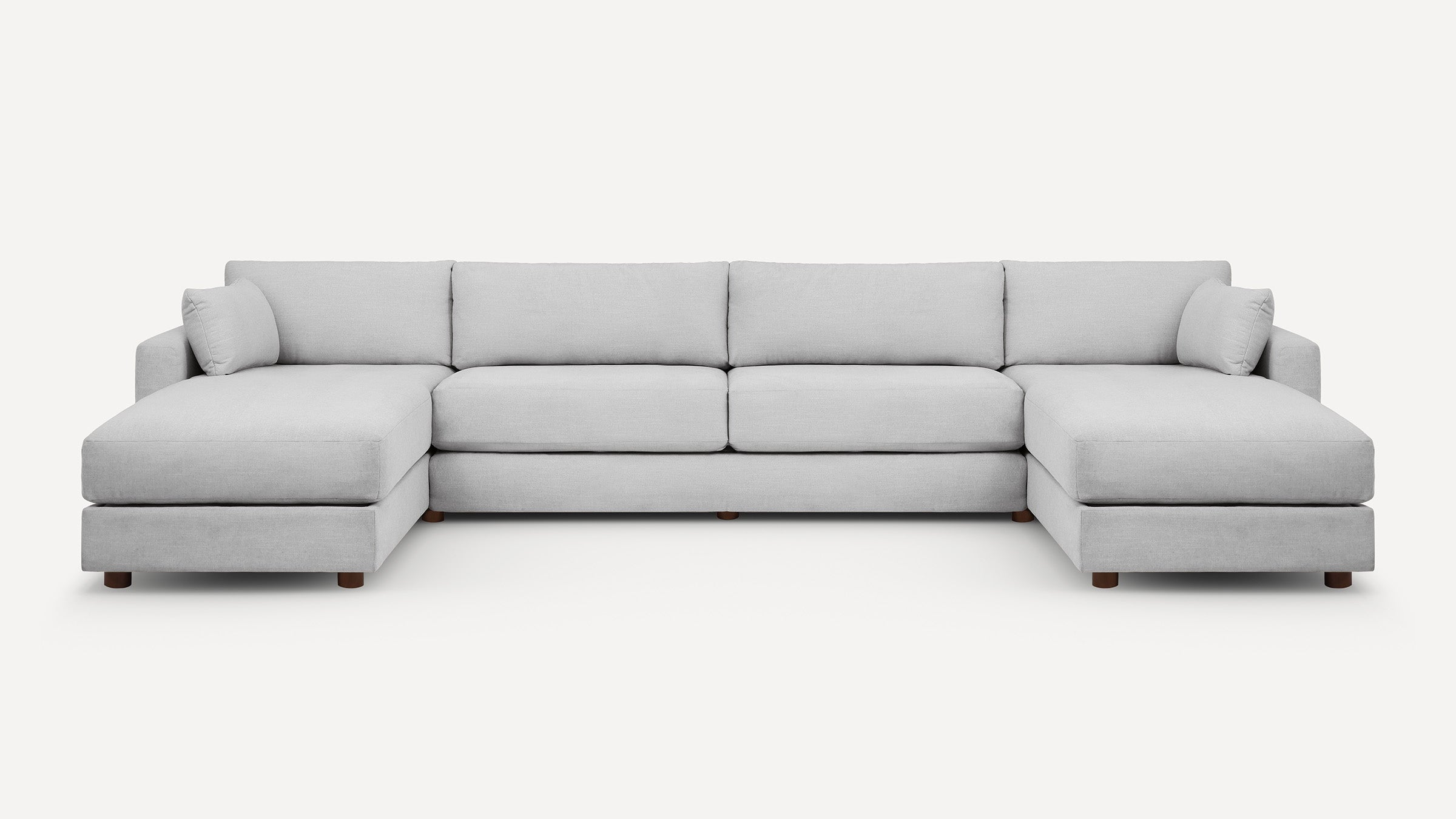 Light grey fabric sectional sofa with one chaise on each end and wooden legs, featuring plush back and side cushions.