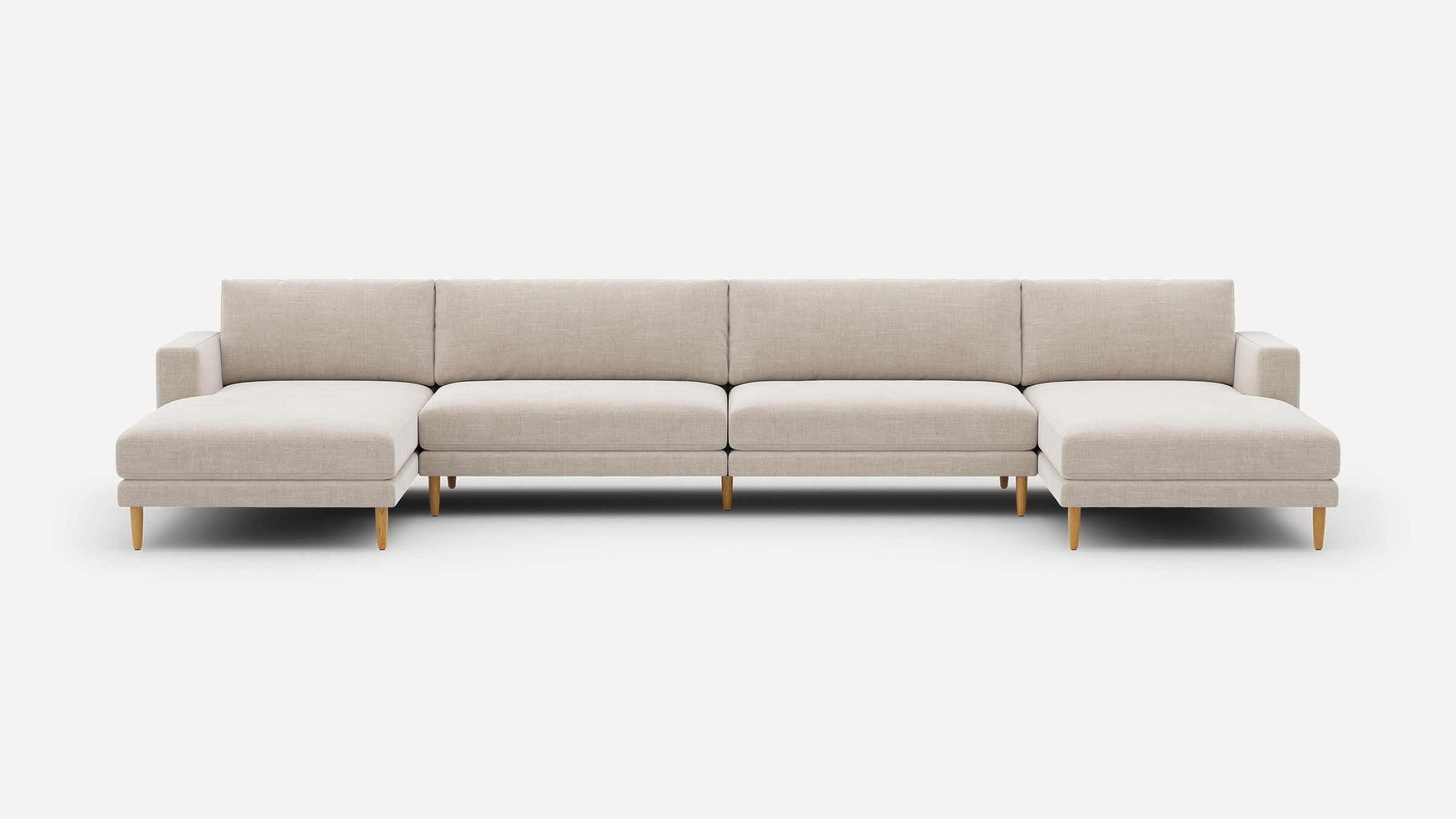 Large, modern beige sectional sofa with wooden legs, featuring left and right chaise lounges and cushioned backrests.