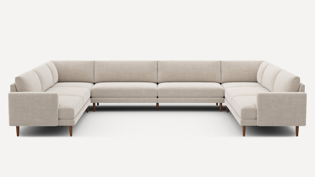 Large U-shaped sectional sofa with beige fabric upholstery, straight arms, cushioned seats, and wooden tapered legs.