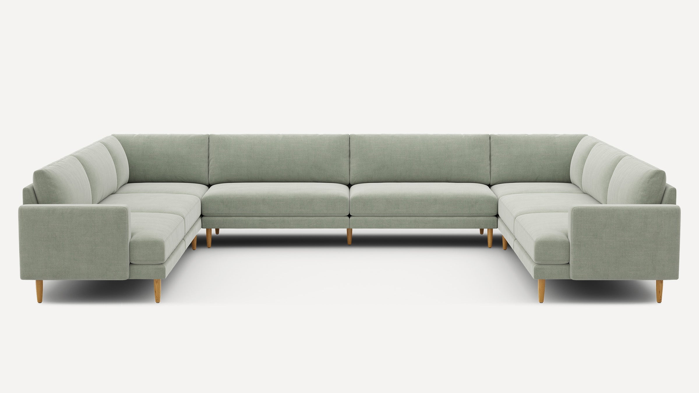 Large U-shaped sectional sofa upholstered in light sage green fabric with straight arms and wooden legs.