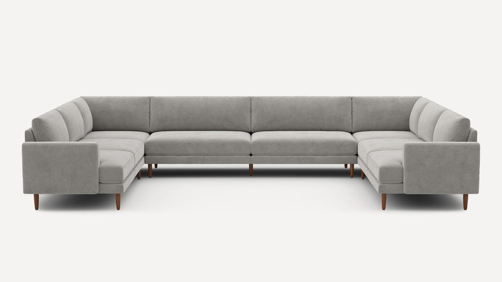 Large U-shaped sectional sofa upholstered in light gray fabric with tufted cushions and wooden tapered legs.