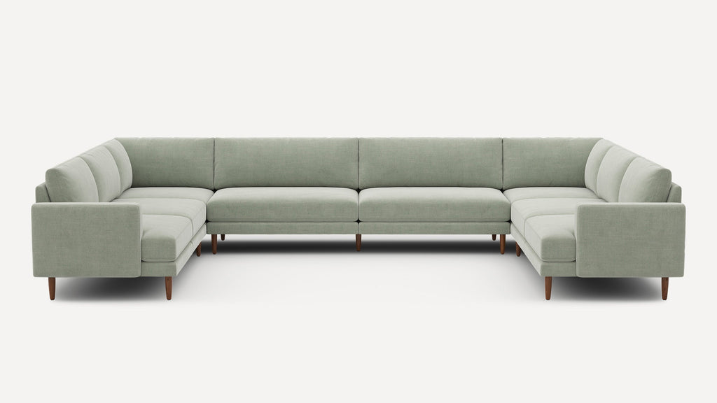 Large U-shaped sectional sofa in light sage green fabric with wooden legs, modern design and clean lines.