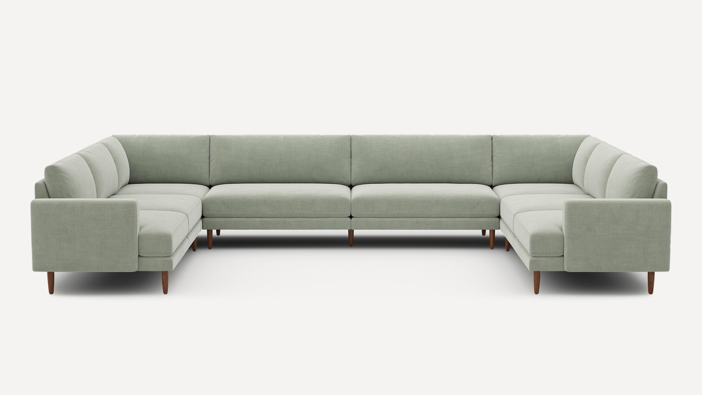 Large U-shaped sectional sofa in light sage green fabric with wooden legs, modern design and clean lines.
