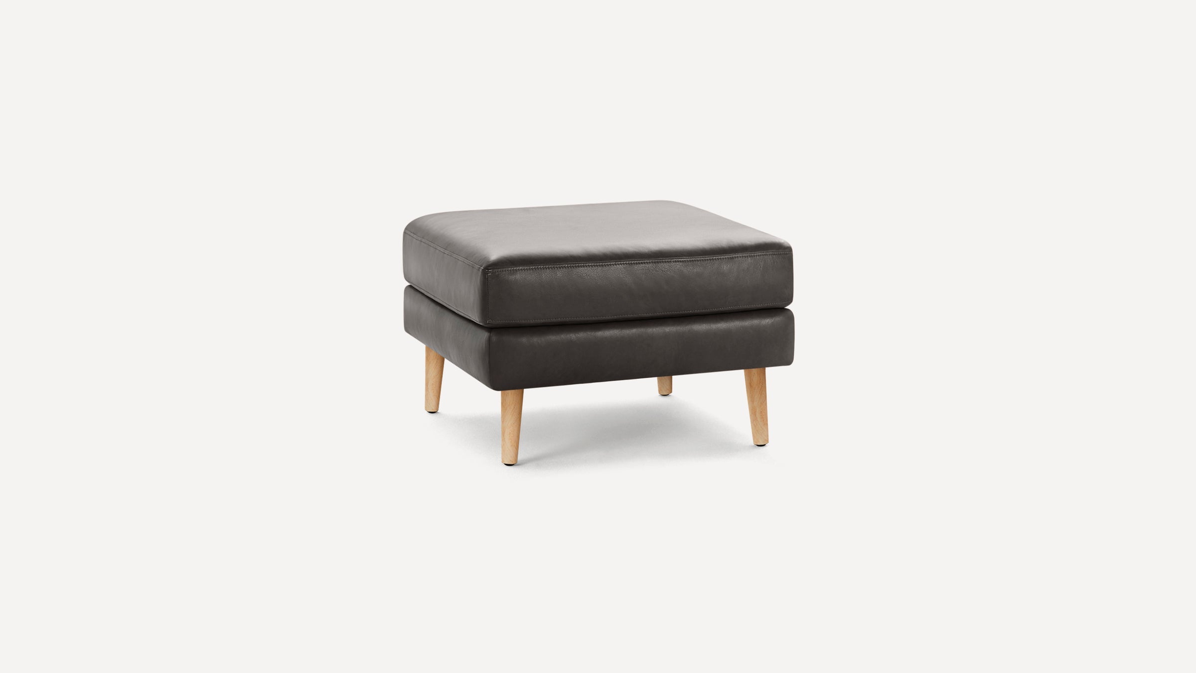 Square black leather ottoman with light wooden tapered legs, featuring cushioned top and minimalistic modern design.
