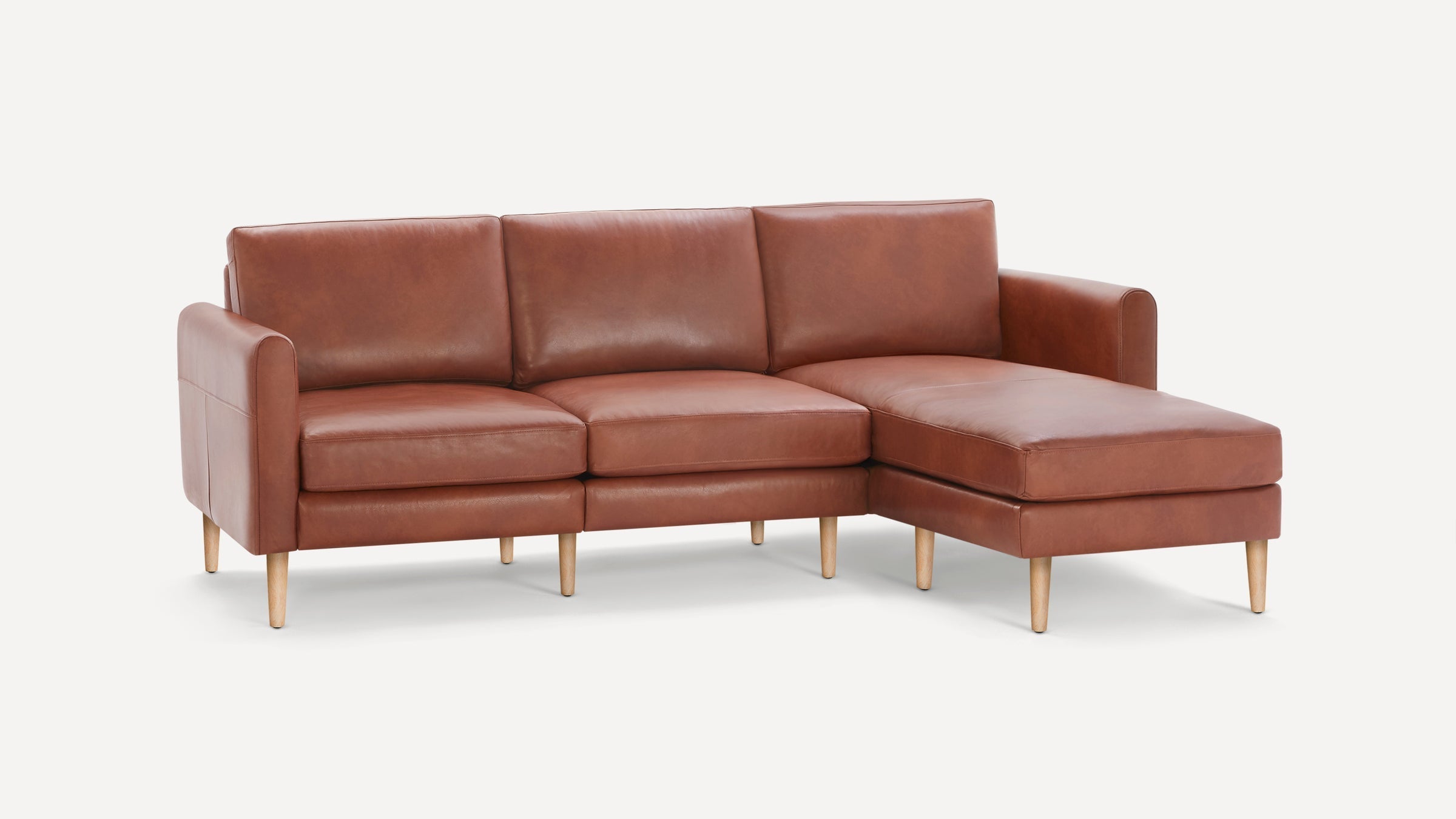 Modern brown leather sectional sofa with three cushions, armrests, and wooden tapered legs, set against a plain white background.