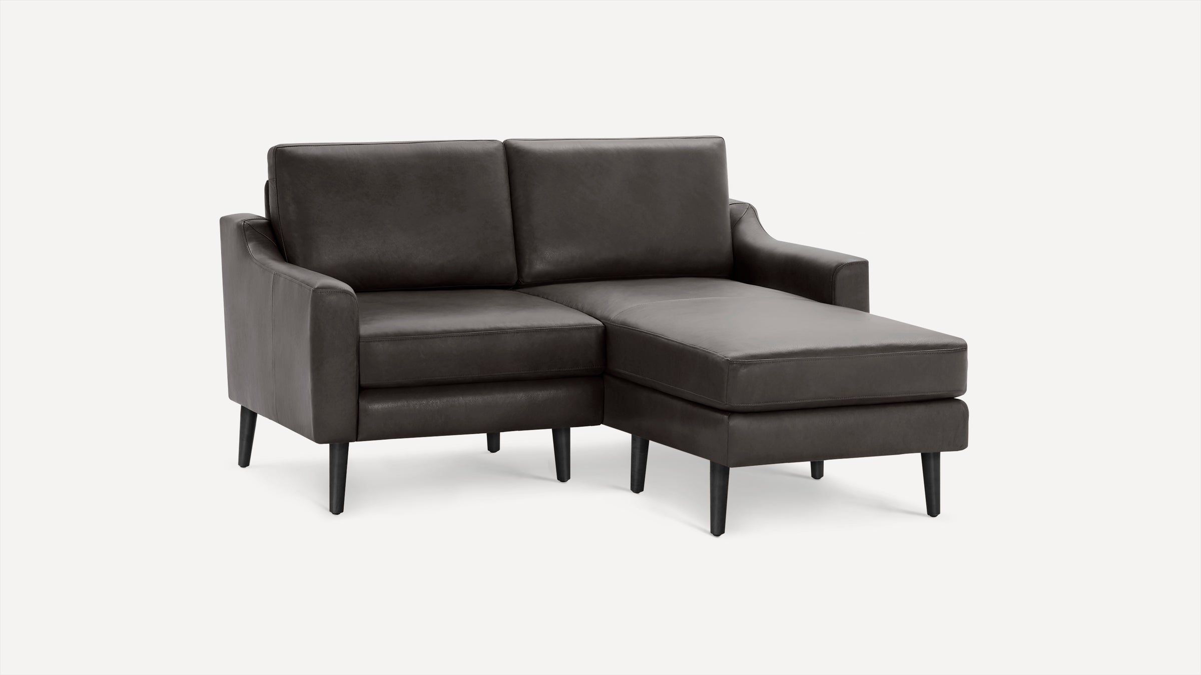 Dark gray leather sectional sofa with chaise lounge on the right side, supported by black tapered wooden legs.