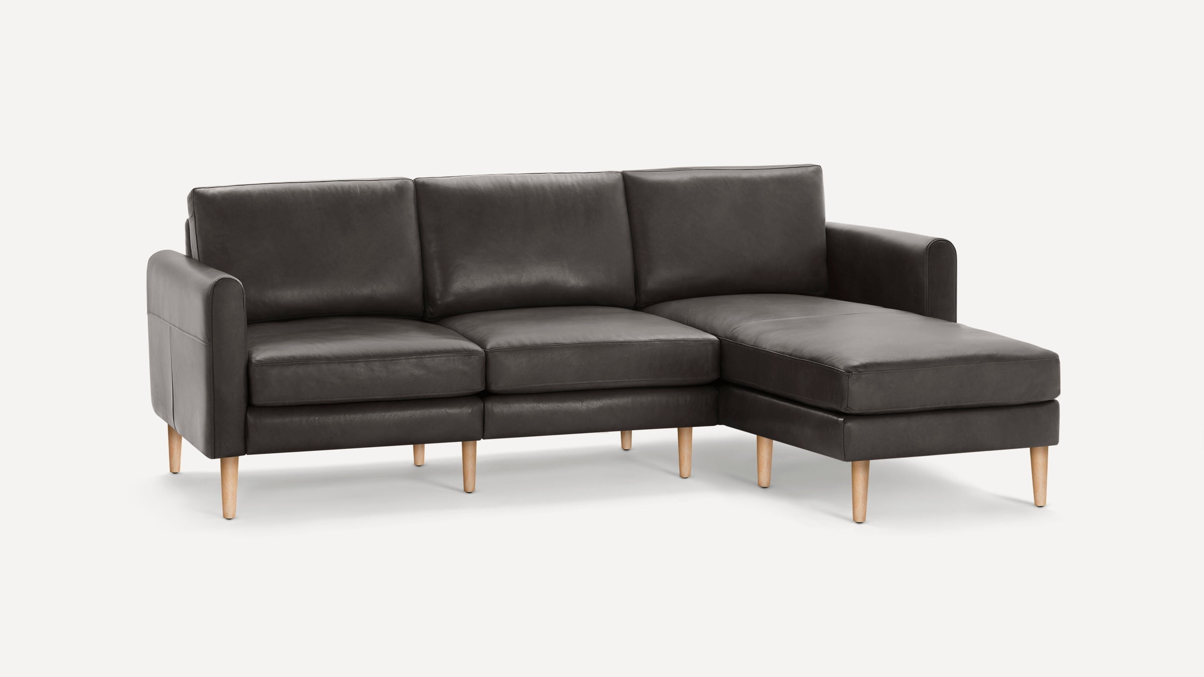 Modern dark gray leather sectional sofa with wooden legs, featuring three seat cushions and a chaise lounge on the right side.