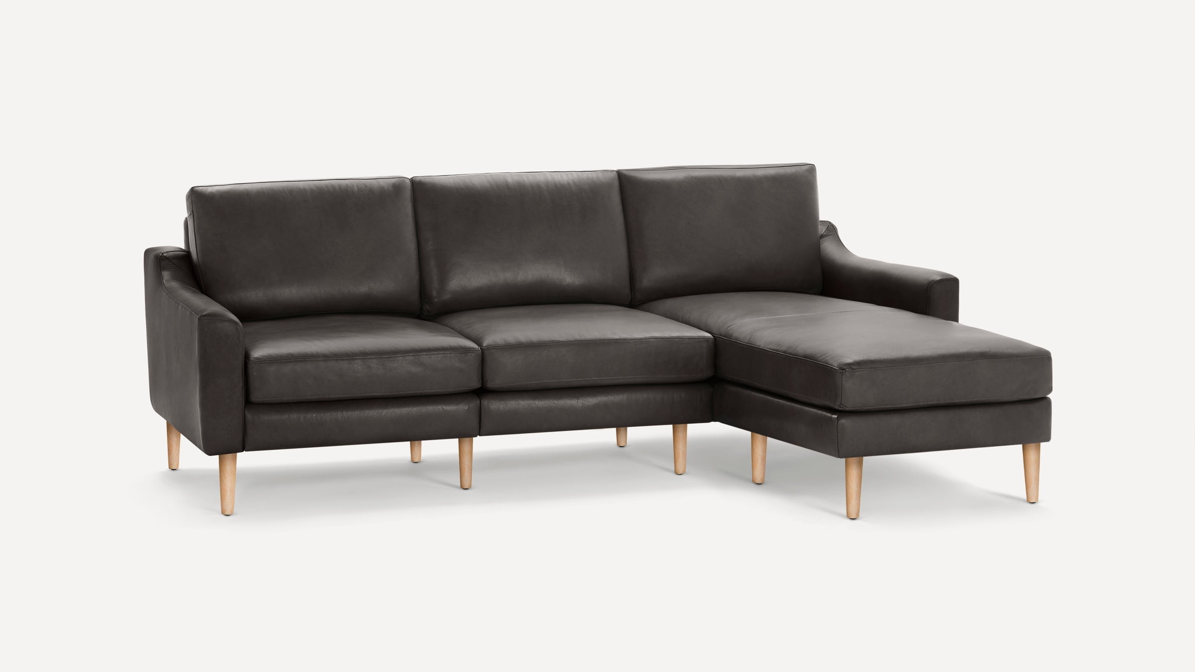 Dark gray leather sectional sofa with wooden legs and a chaise lounge on the right side, set against a white background.