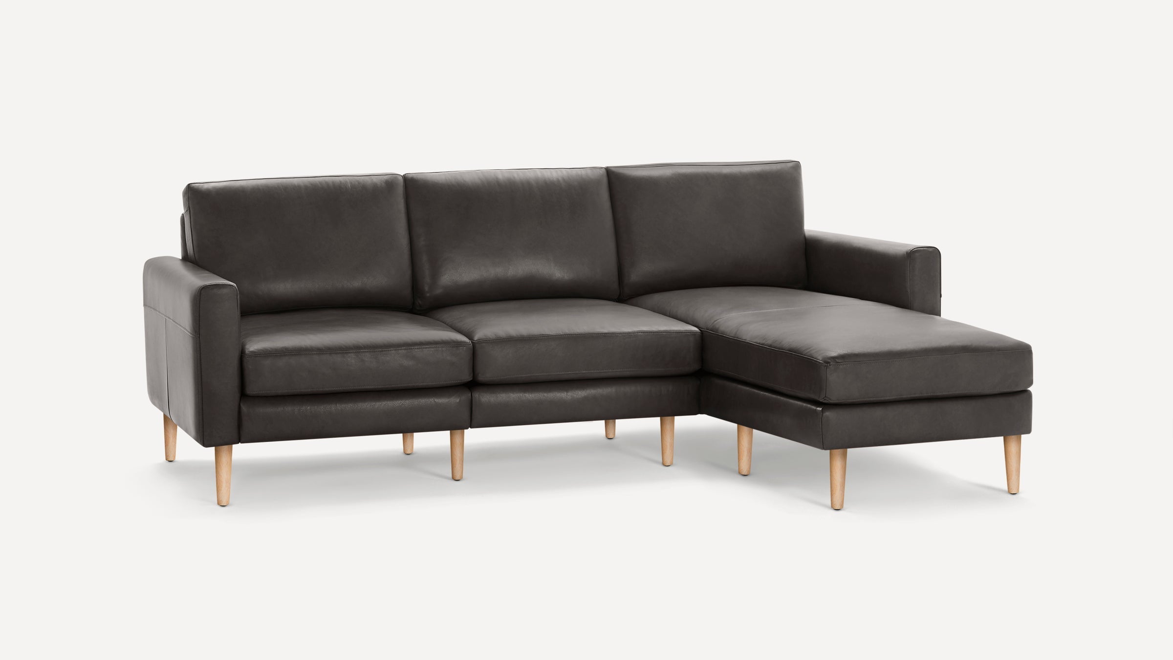 Modern dark gray leather sectional sofa with wooden legs and chaise lounge on the right side, set against a white background.