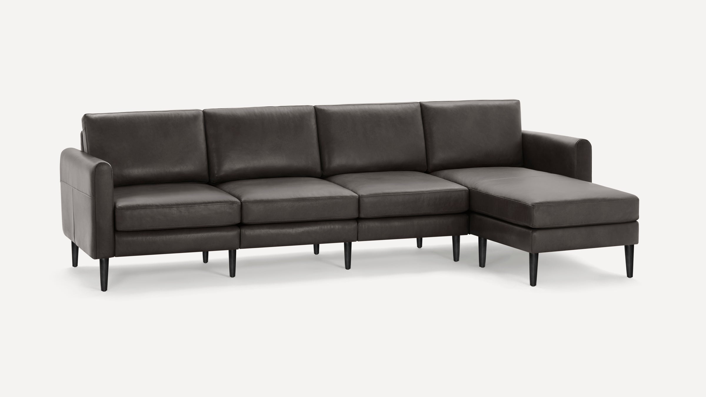 Dark gray leather sectional sofa with sleek cushions, straight arms, and tapered black wooden legs, featuring a chaise lounge on the right side.