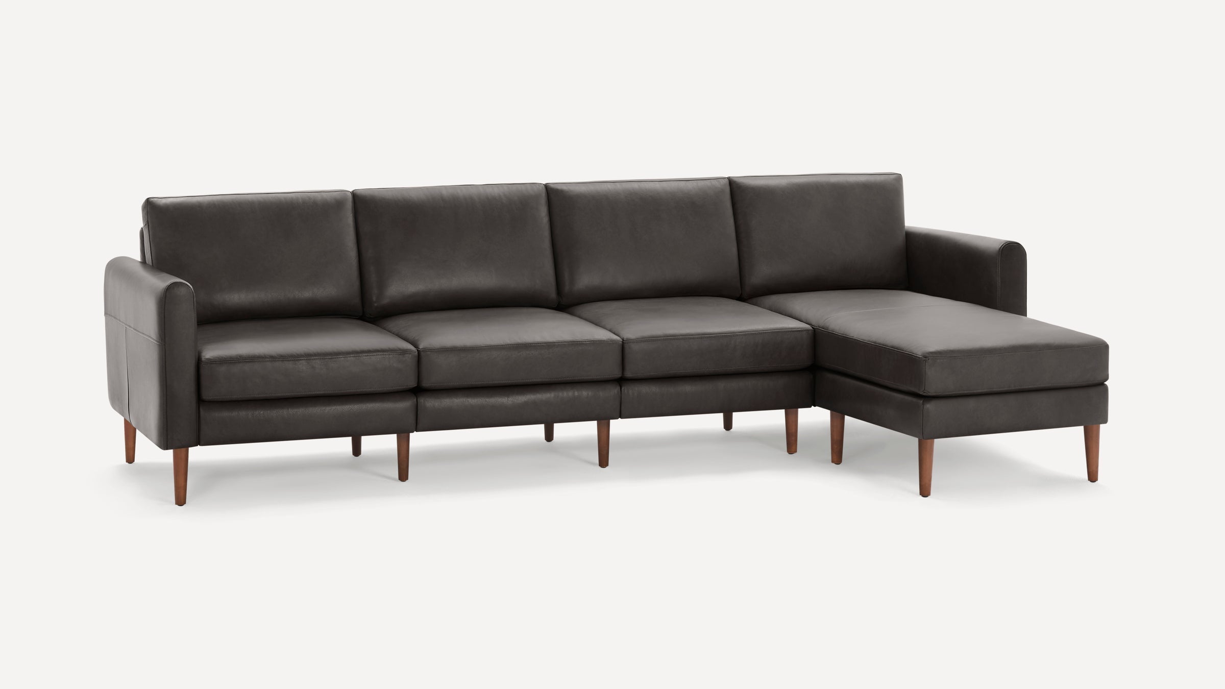 Modern dark gray leather sectional sofa with wooden legs and chaise lounge on right side, set against a white background.