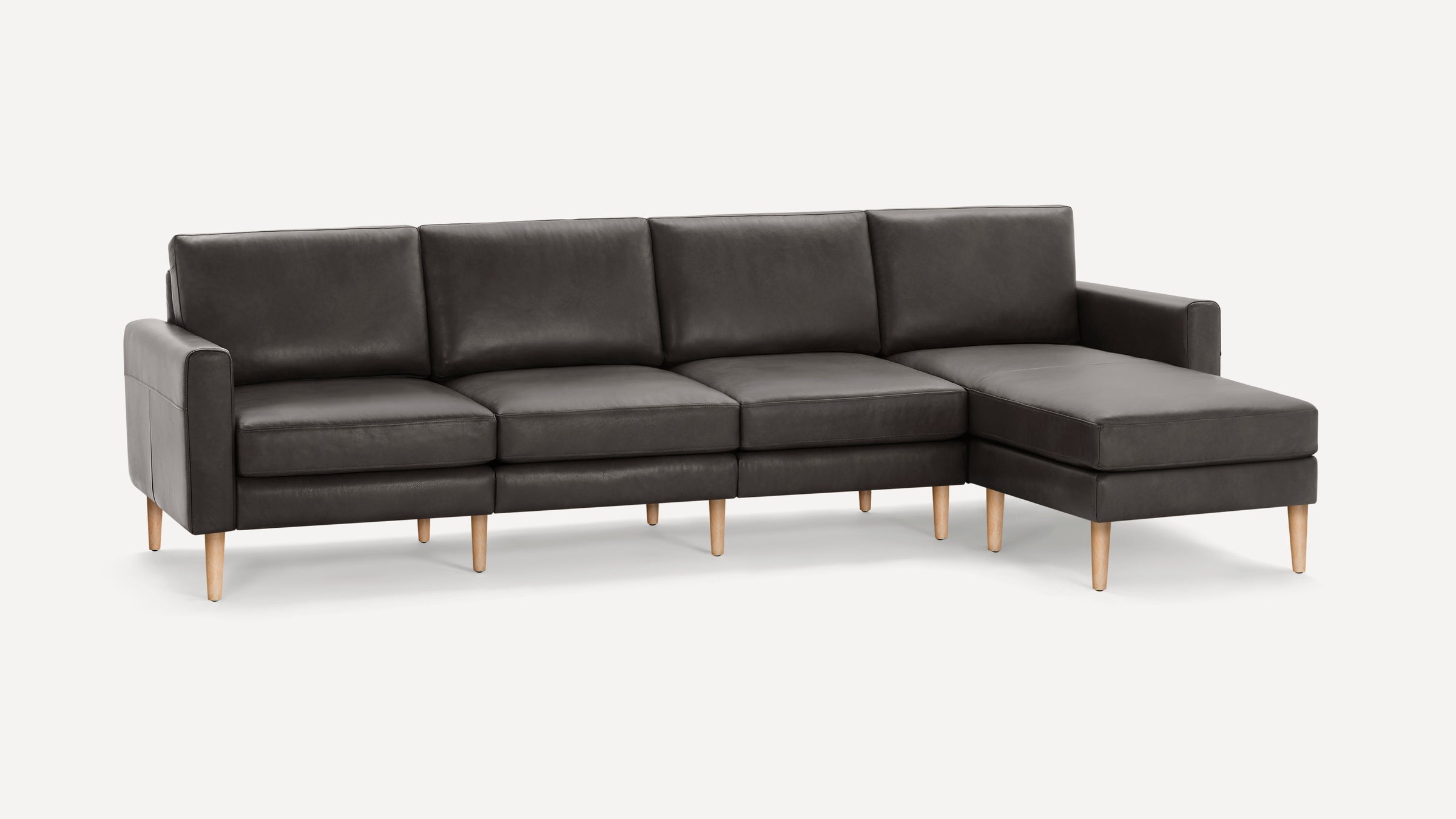 Modern dark gray leather sectional sofa with chaise lounge and light wooden legs, featuring clean lines and cushioned seats.