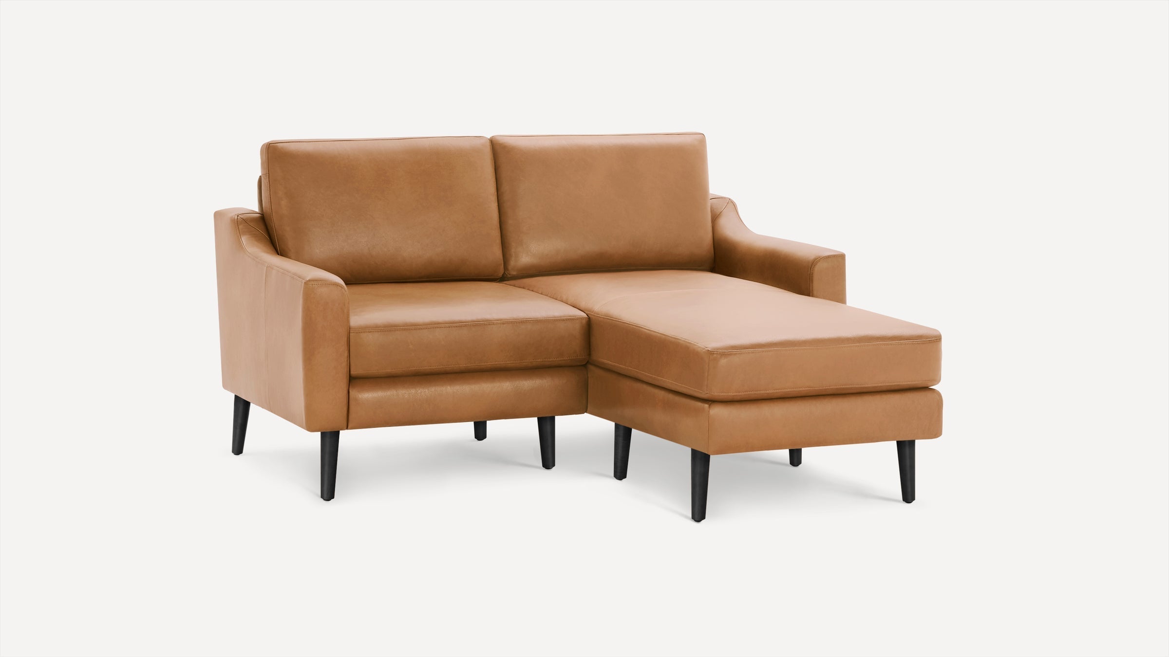 Modern tan leather sectional sofa with chaise lounge and black tapered legs on a plain white background.