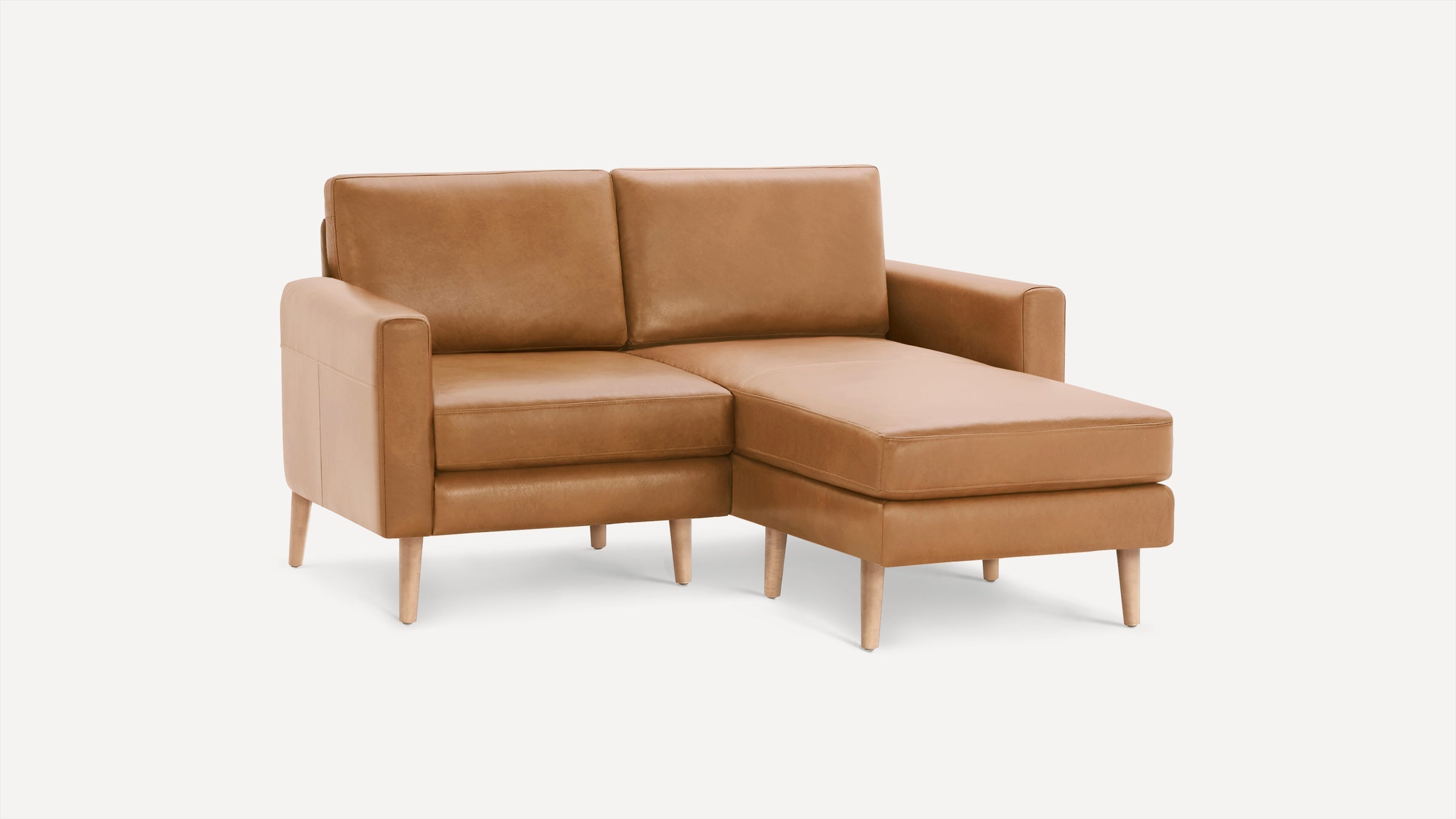Modern camel brown leather sectional sofa with chaise lounge and light wood tapered legs on white background.
