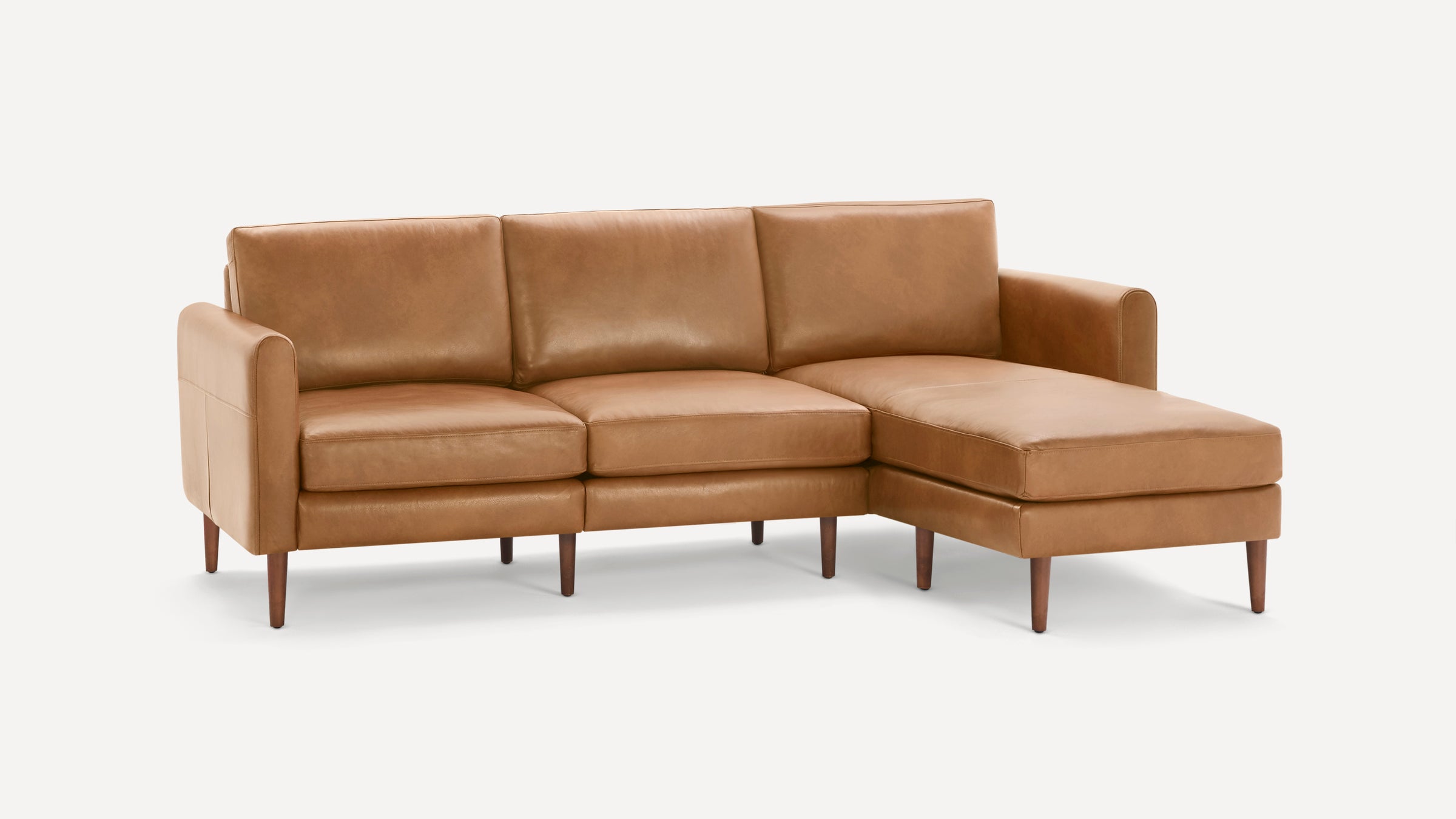 Mid-century style tan leather sectional sofa with right-side chaise and wooden tapered legs on white background.
