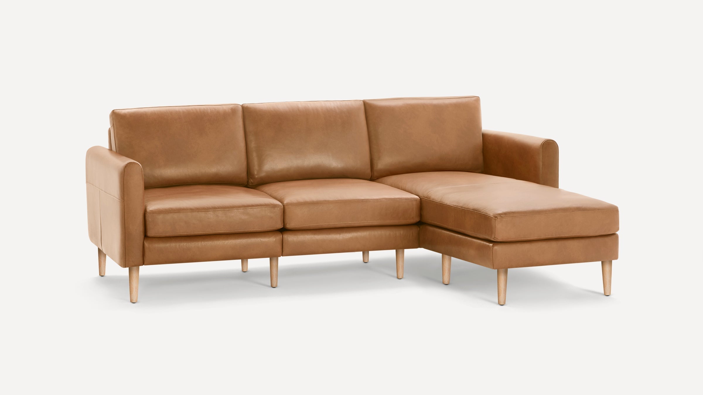 Tan leather sectional sofa with three seat cushions, a chaise lounge on the right side, and wooden tapered legs.