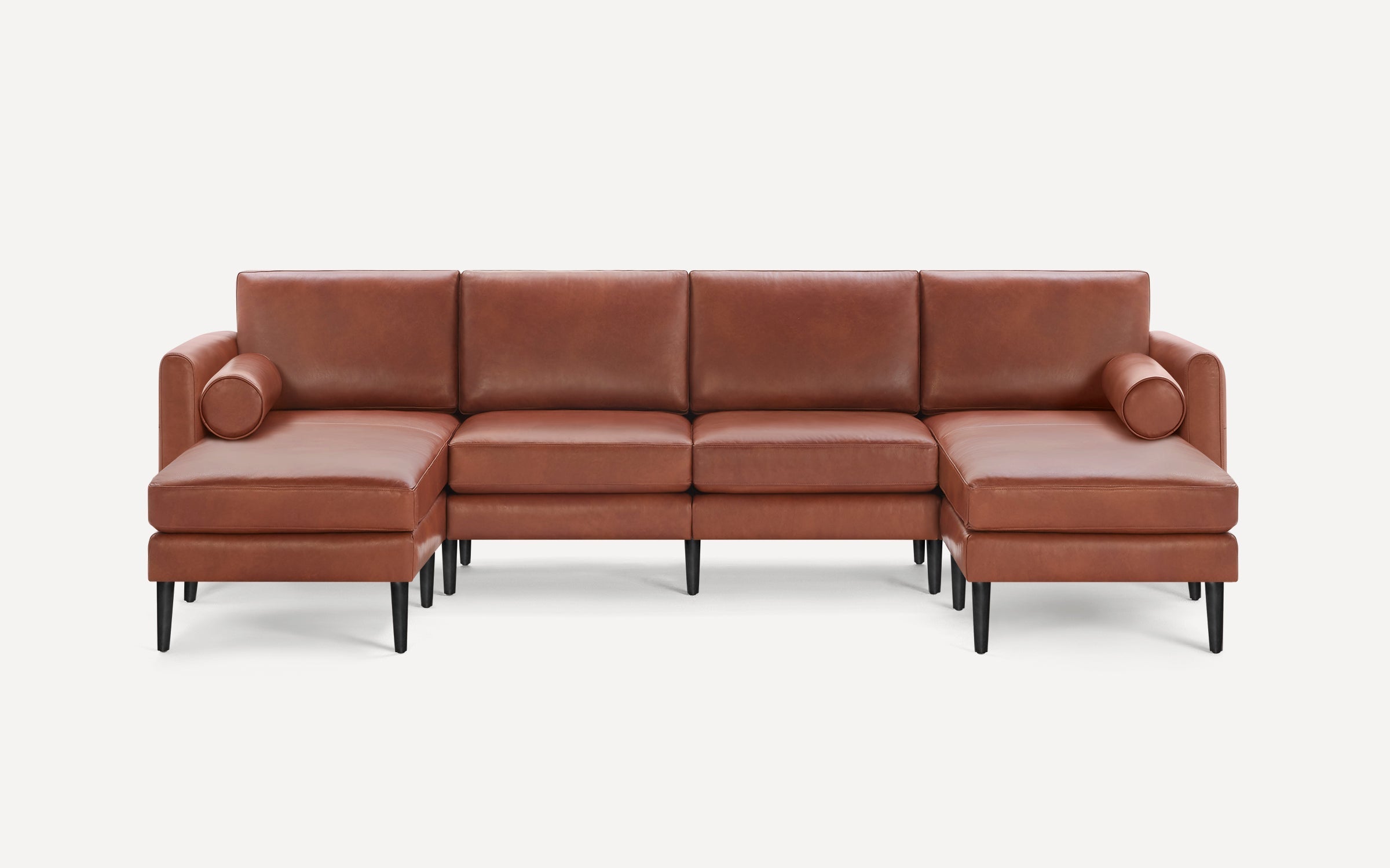 Brown leather U-shaped sectional sofa with black tapered legs and two cylindrical bolster pillows on each end.