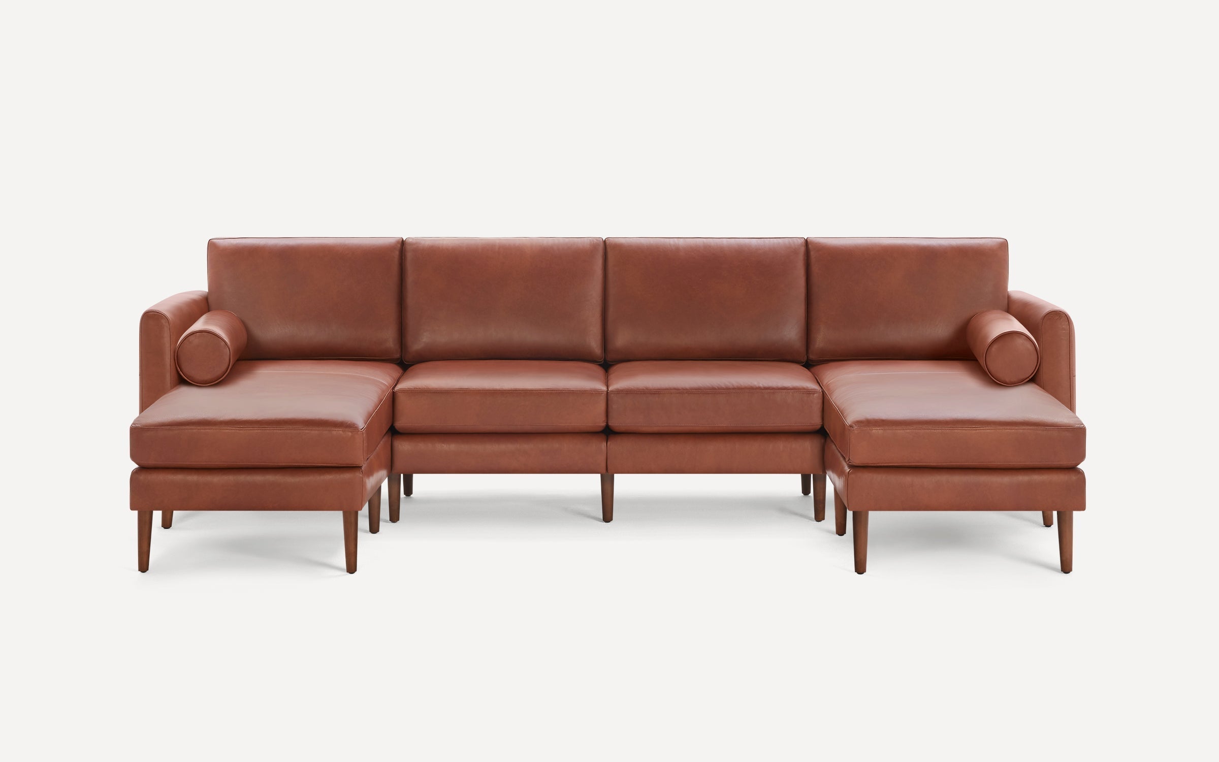 Brown leather sectional sofa with wooden legs, featuring chaise lounges on both ends and cylindrical bolster pillows.