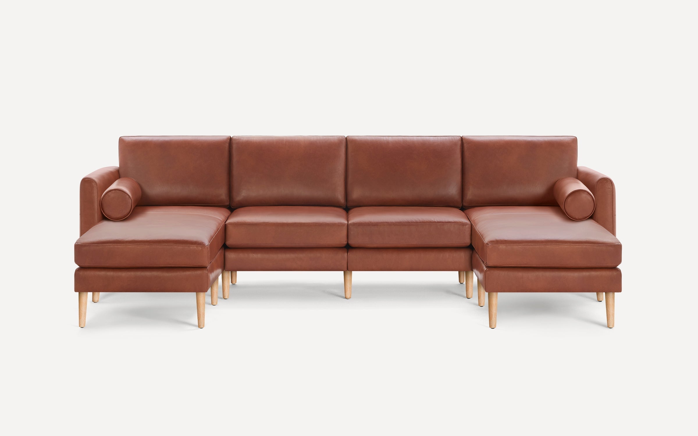 Brown leather U-shaped sectional sofa with wooden legs and two cylindrical bolster pillows on each end.