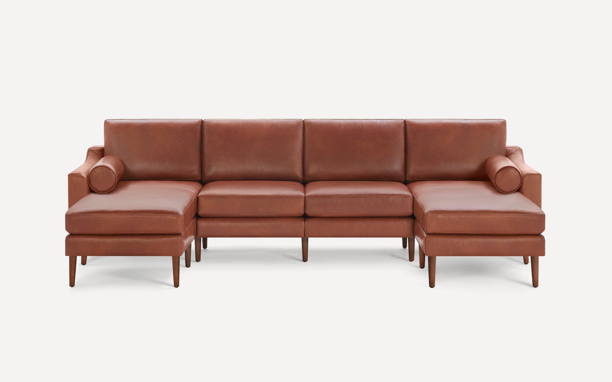 Modern brown leather sectional sofa with clean lines, wooden legs, and two cylindrical bolster pillows on each end.