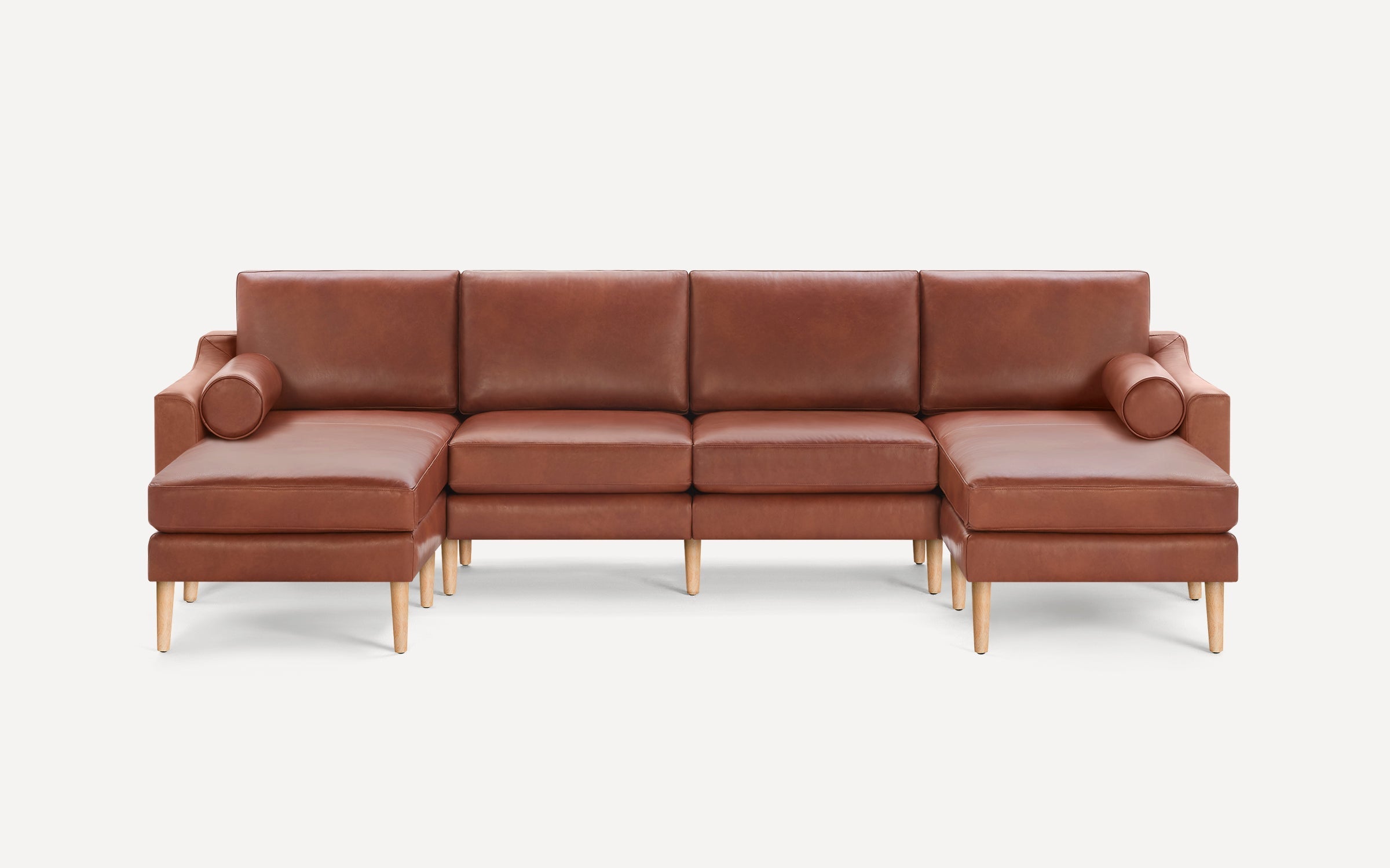 Brown leather sectional sofa with wooden tapered legs, featuring two chaise lounges and two cylindrical bolster pillows.