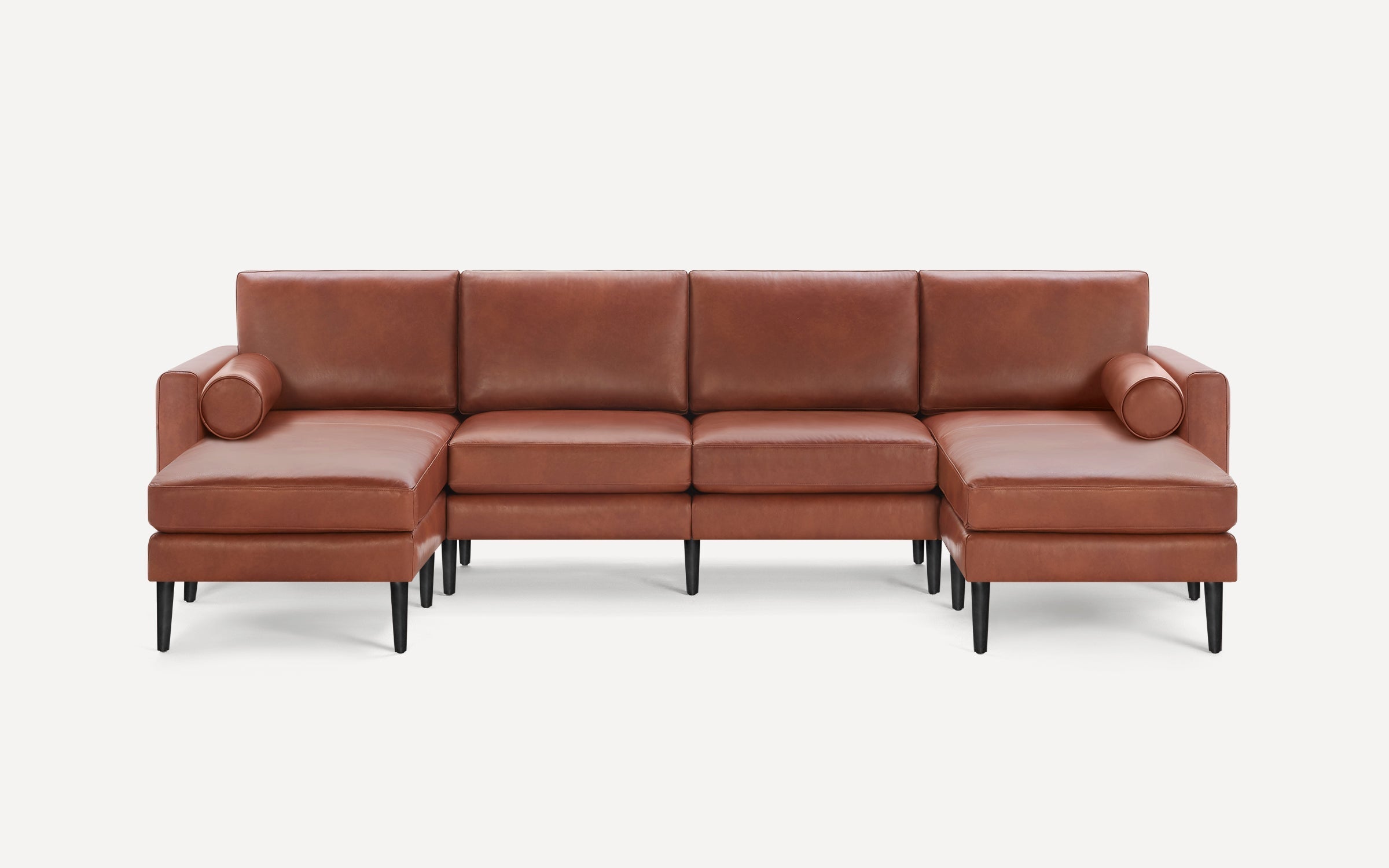 Modern sectional sofa with brown leather upholstery, black tapered legs, and two matching cylindrical bolster pillows.