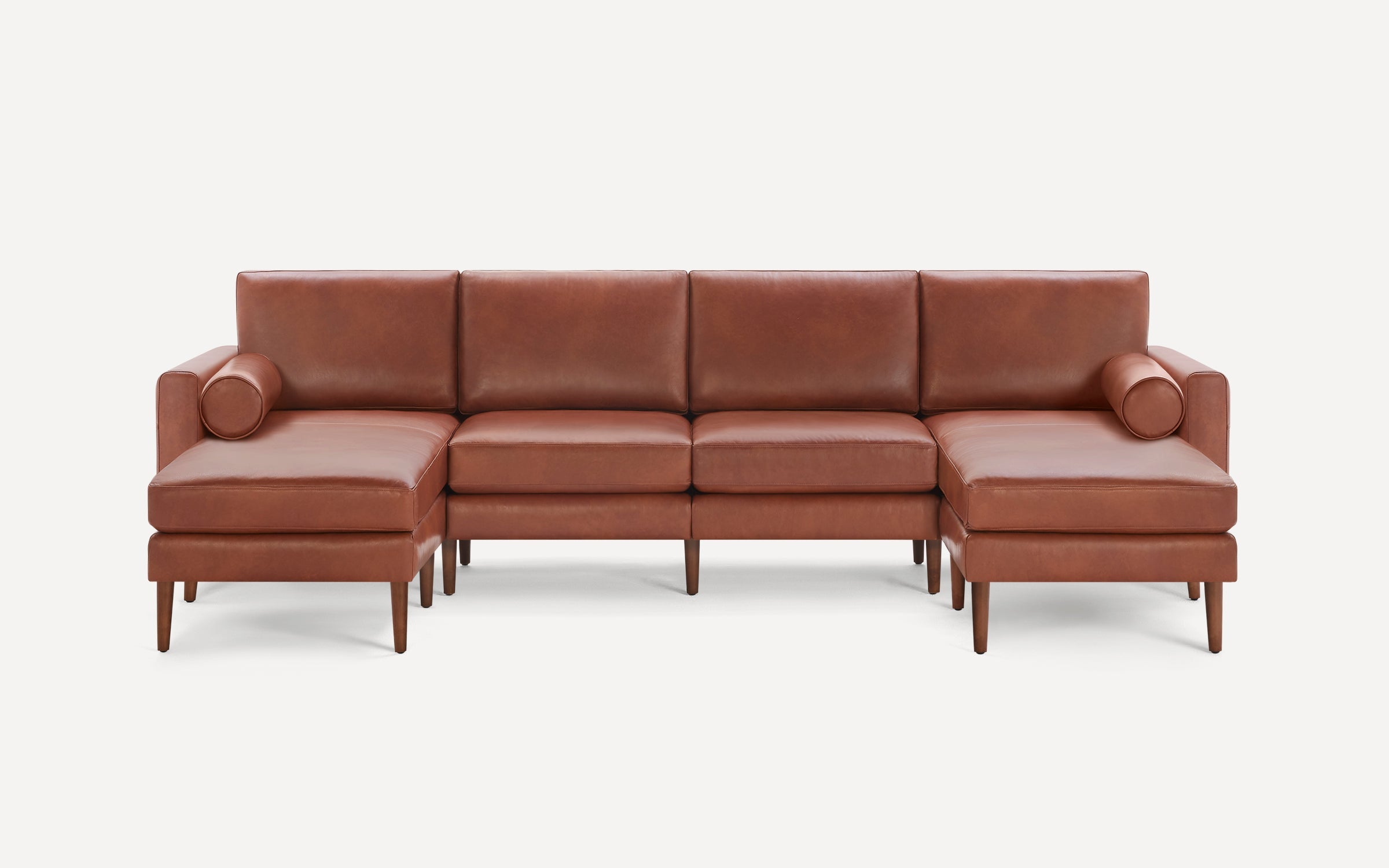 Mid-century modern brown leather sectional sofa with wooden legs, two chaise lounges, and cylindrical bolster pillows.