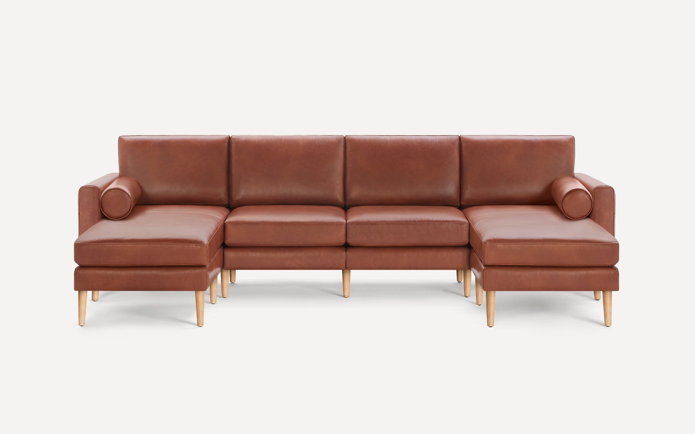 Modern brown leather sectional sofa with wooden legs, featuring chaise lounges on both sides and cylindrical bolster pillows.