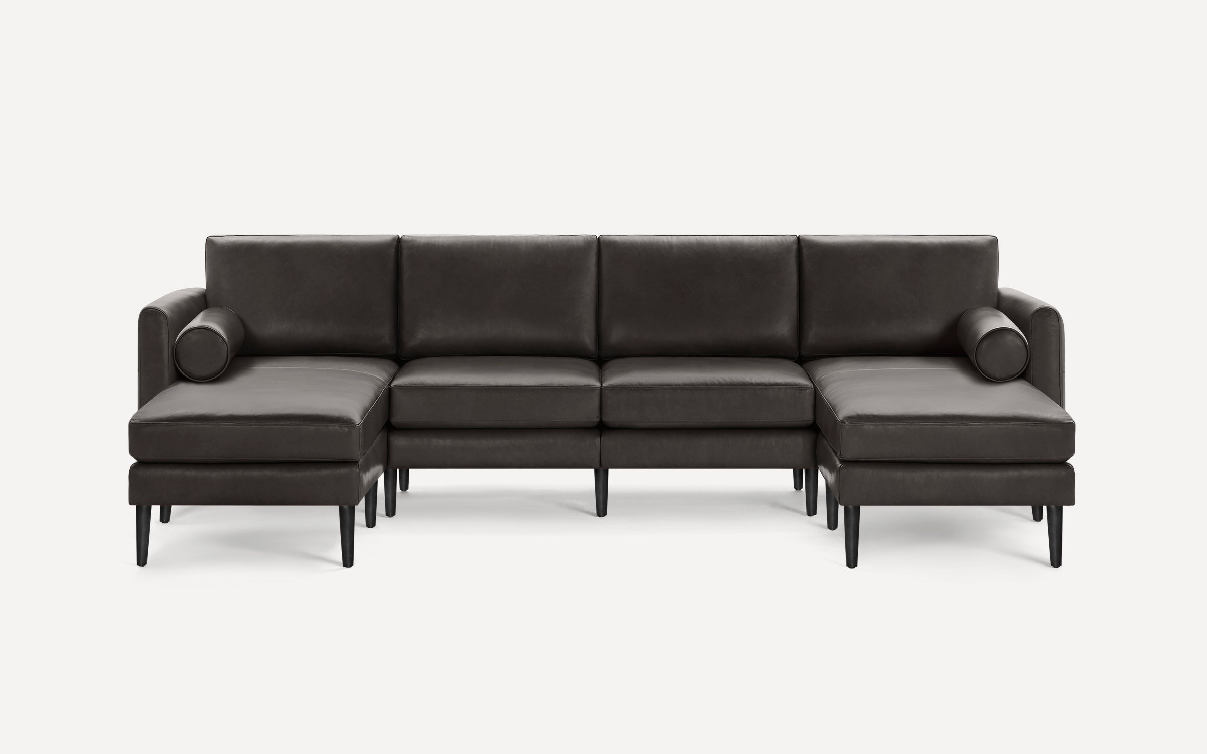 Modern dark brown leather U-shaped sectional sofa with black wooden legs and two round bolster pillows on each end.