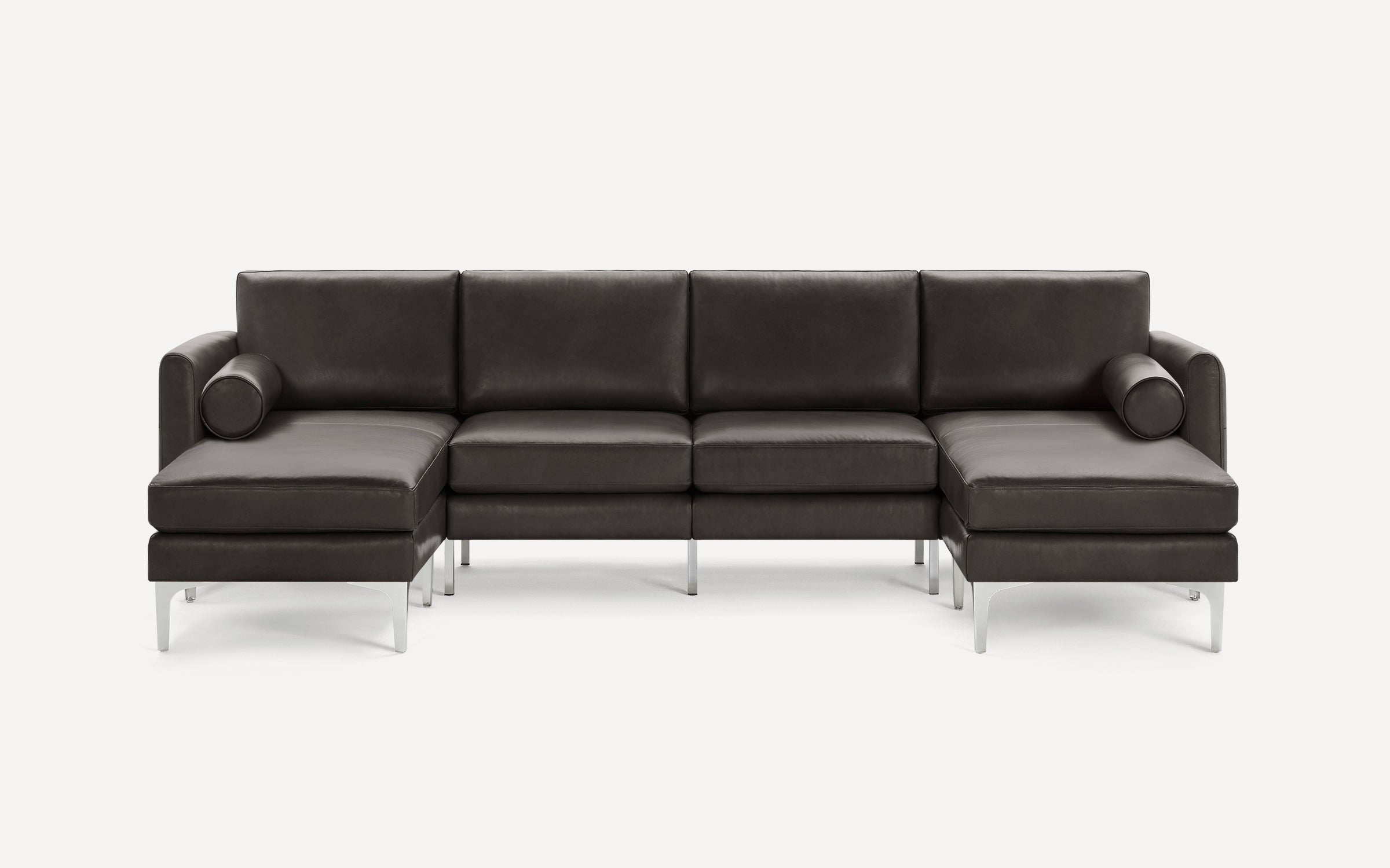 Modern dark gray leather sectional sofa with metal legs, featuring two chaise lounges and cylindrical bolster pillows on each side.