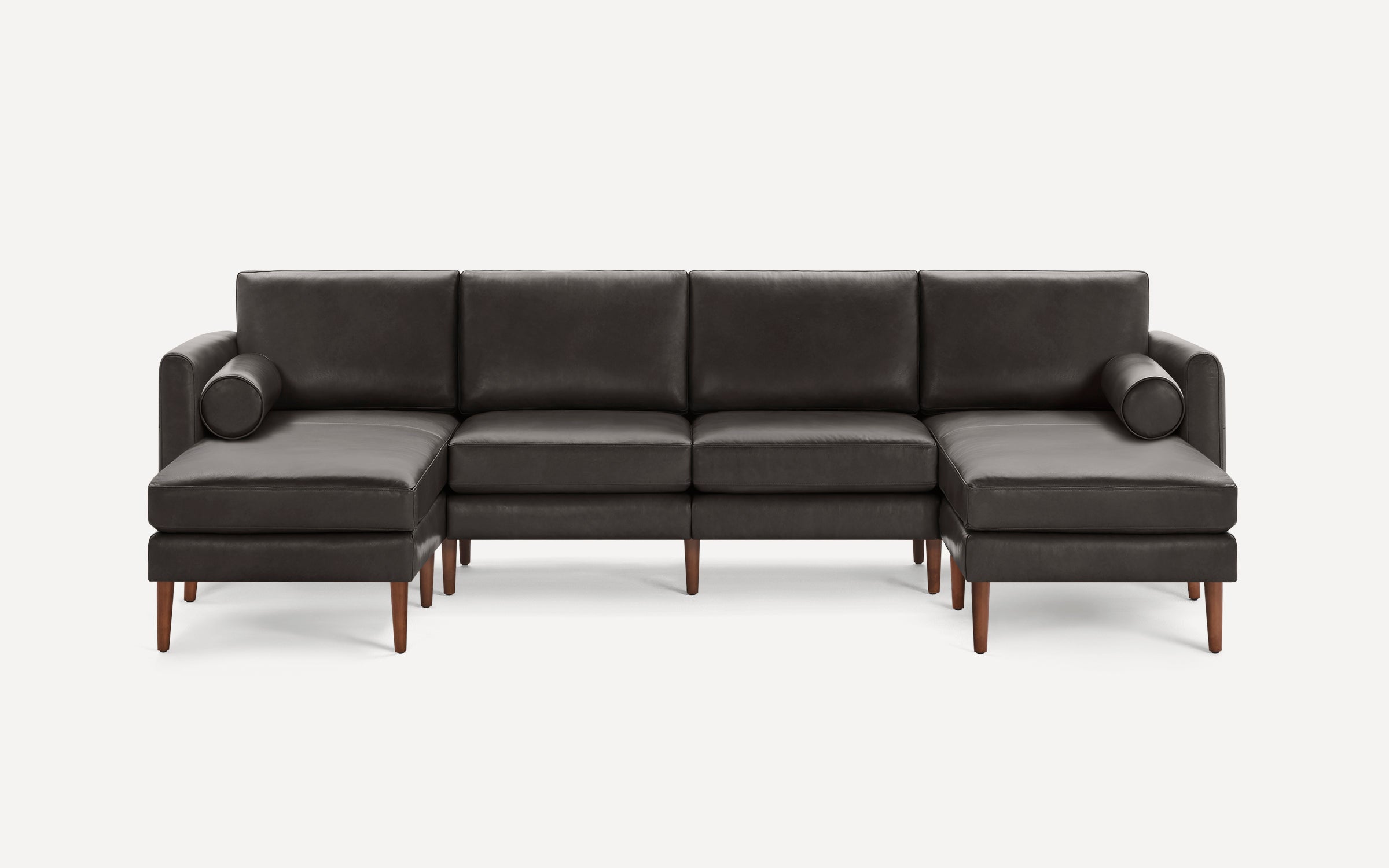 Modern dark gray leather sectional sofa with two chaise lounges, cylindrical bolster pillows, and wooden legs.