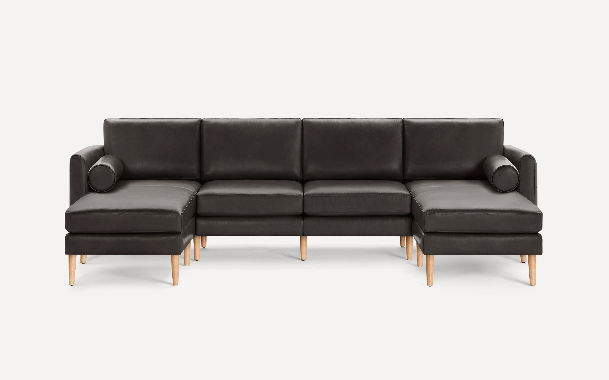 Modern large dark gray leather sectional sofa with wooden legs and two cylindrical bolster pillows on each side.