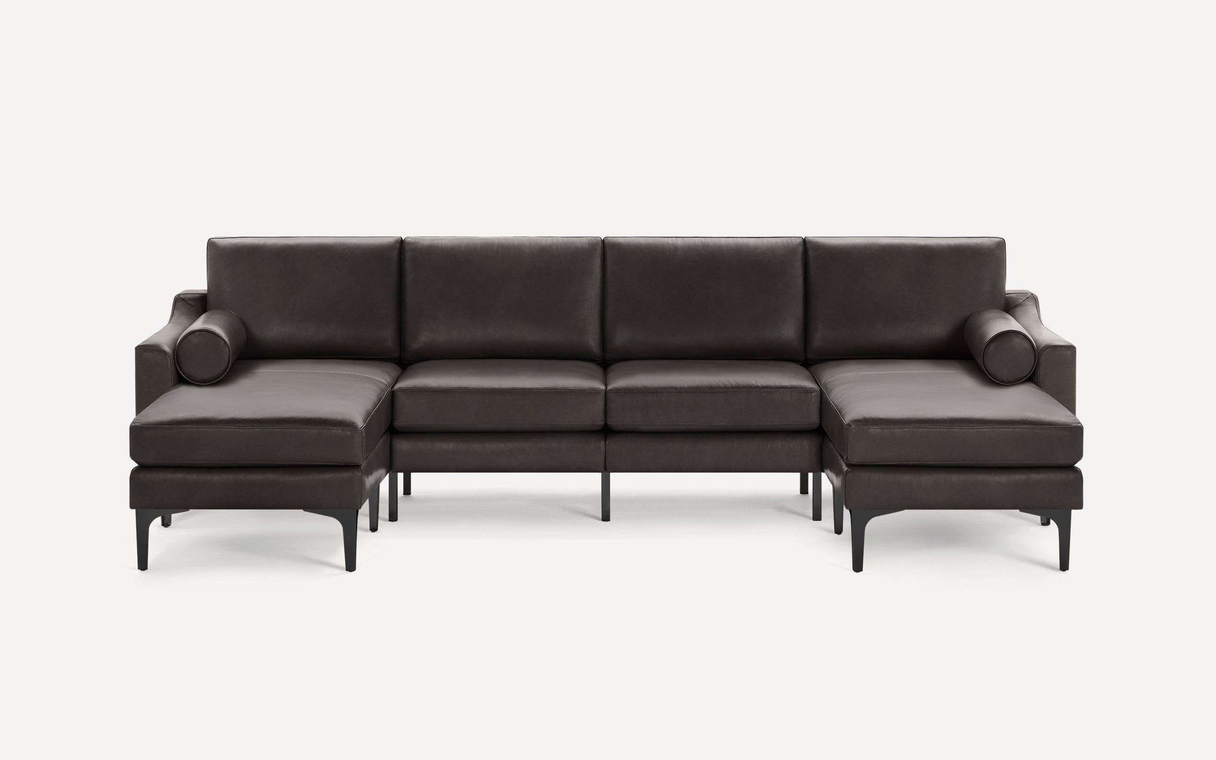 Modern dark gray leather sectional sofa with clean lines, back cushions, cylindrical bolster pillows, and black metal legs on white background.