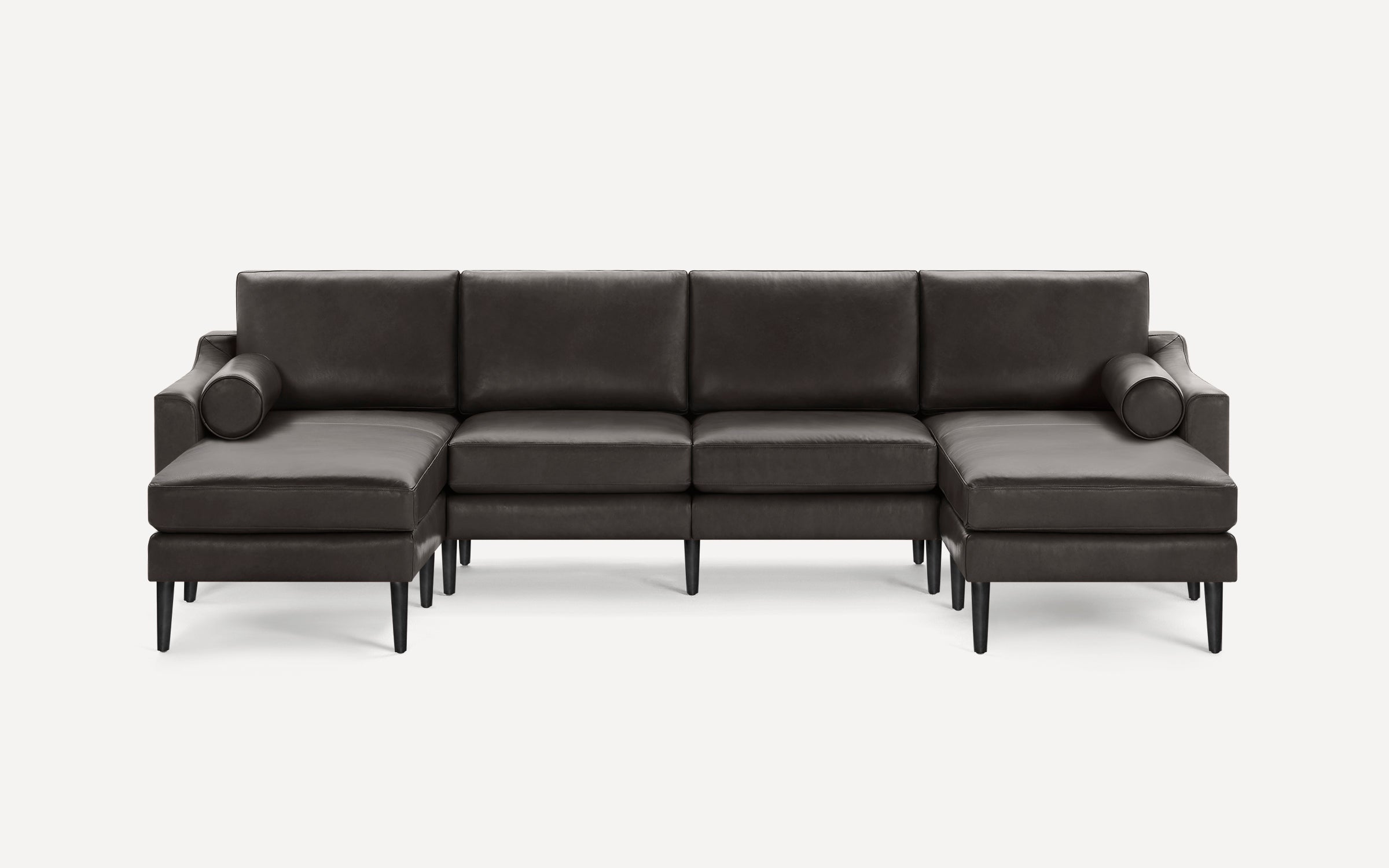A modern dark gray sectional sofa with clean lines, high back cushions, angled black legs, and two cylindrical bolster pillows.