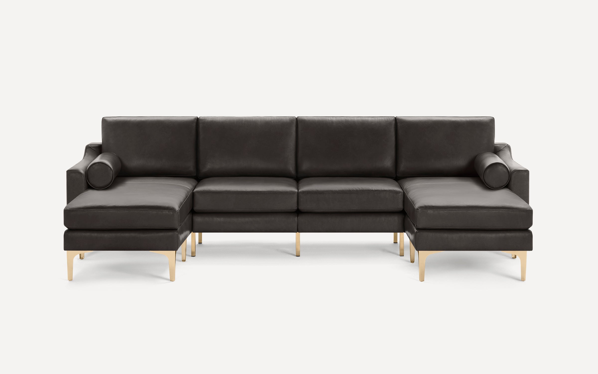 Dark gray leather sectional sofa with gold metal legs, L-shaped design, and matching cylindrical bolster pillows on each end.