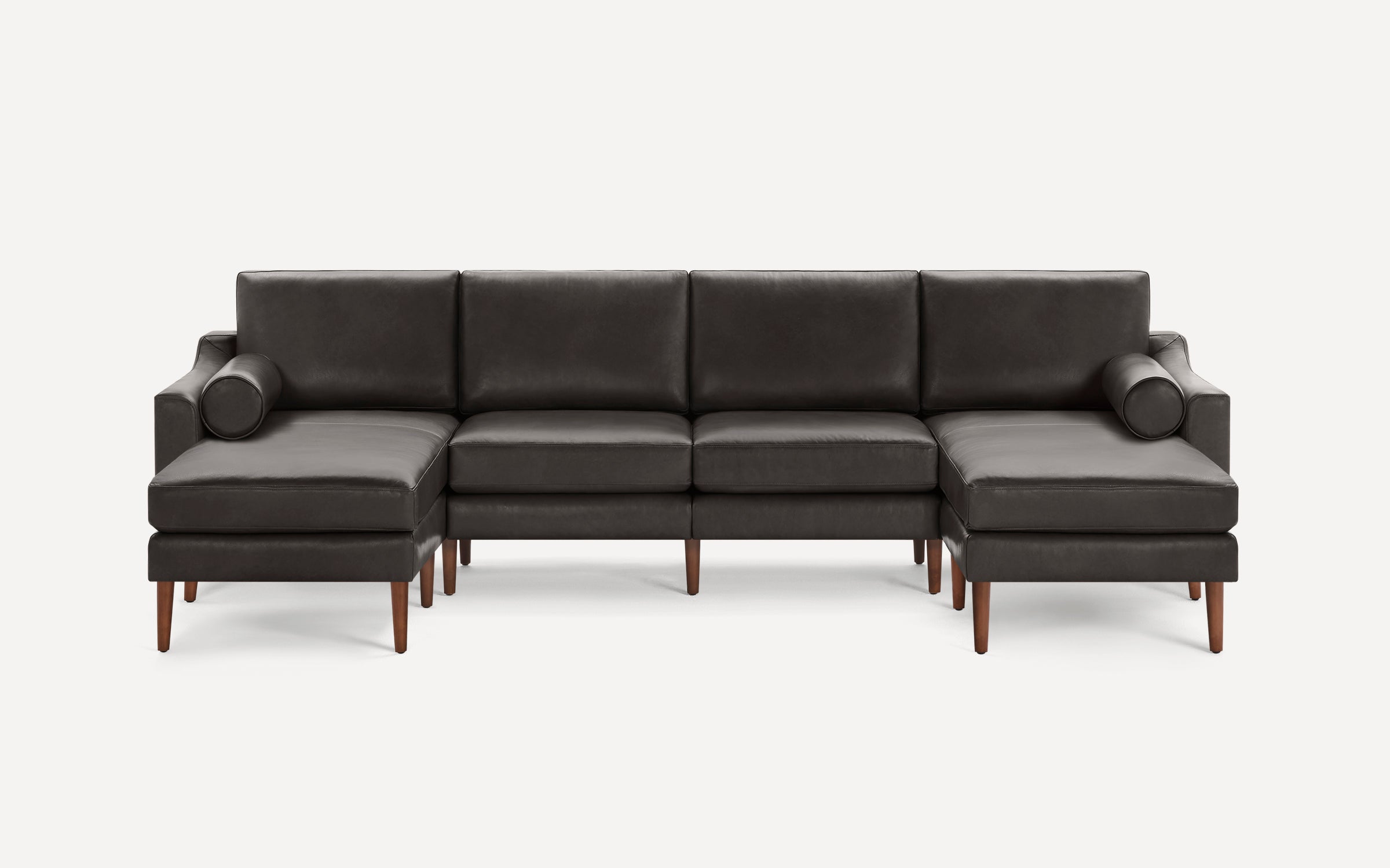 Modern dark gray leather sectional sofa with wooden legs, featuring two chaise ends and cylindrical lumbar pillows.