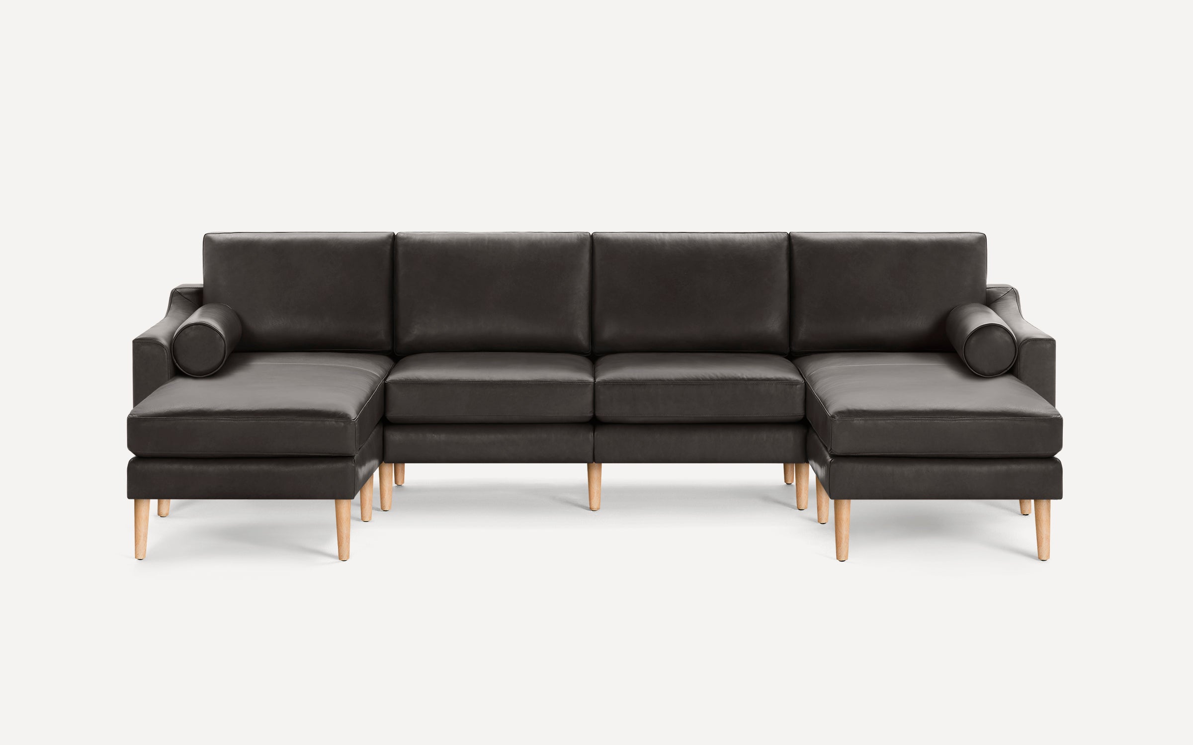 Dark gray leather sectional sofa with wooden tapered legs and cylindrical bolster pillows on each end.