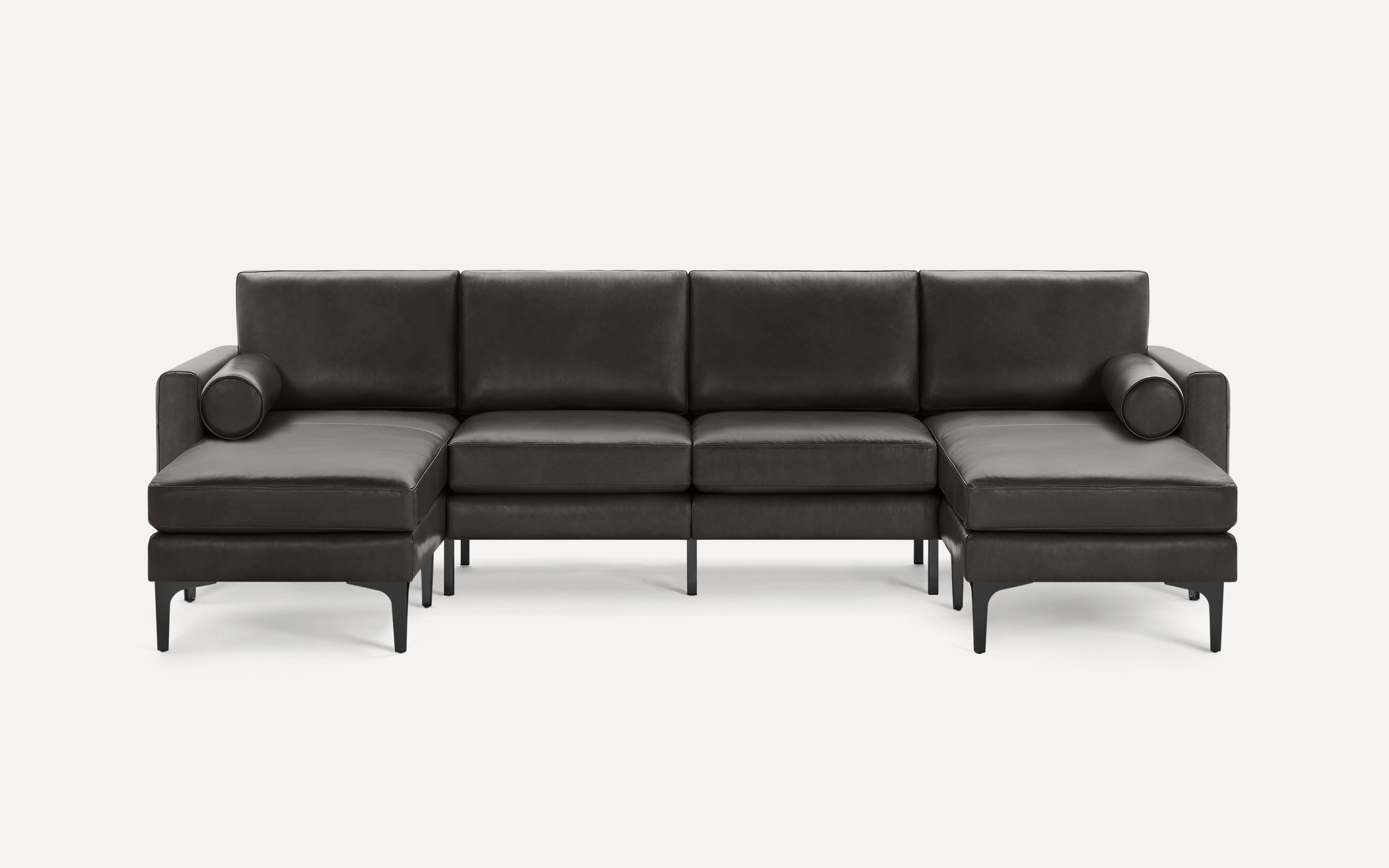 Modern dark gray leather sectional sofa with slim black metal legs, featuring two chaise lounges and cylindrical bolster pillows on each end.
